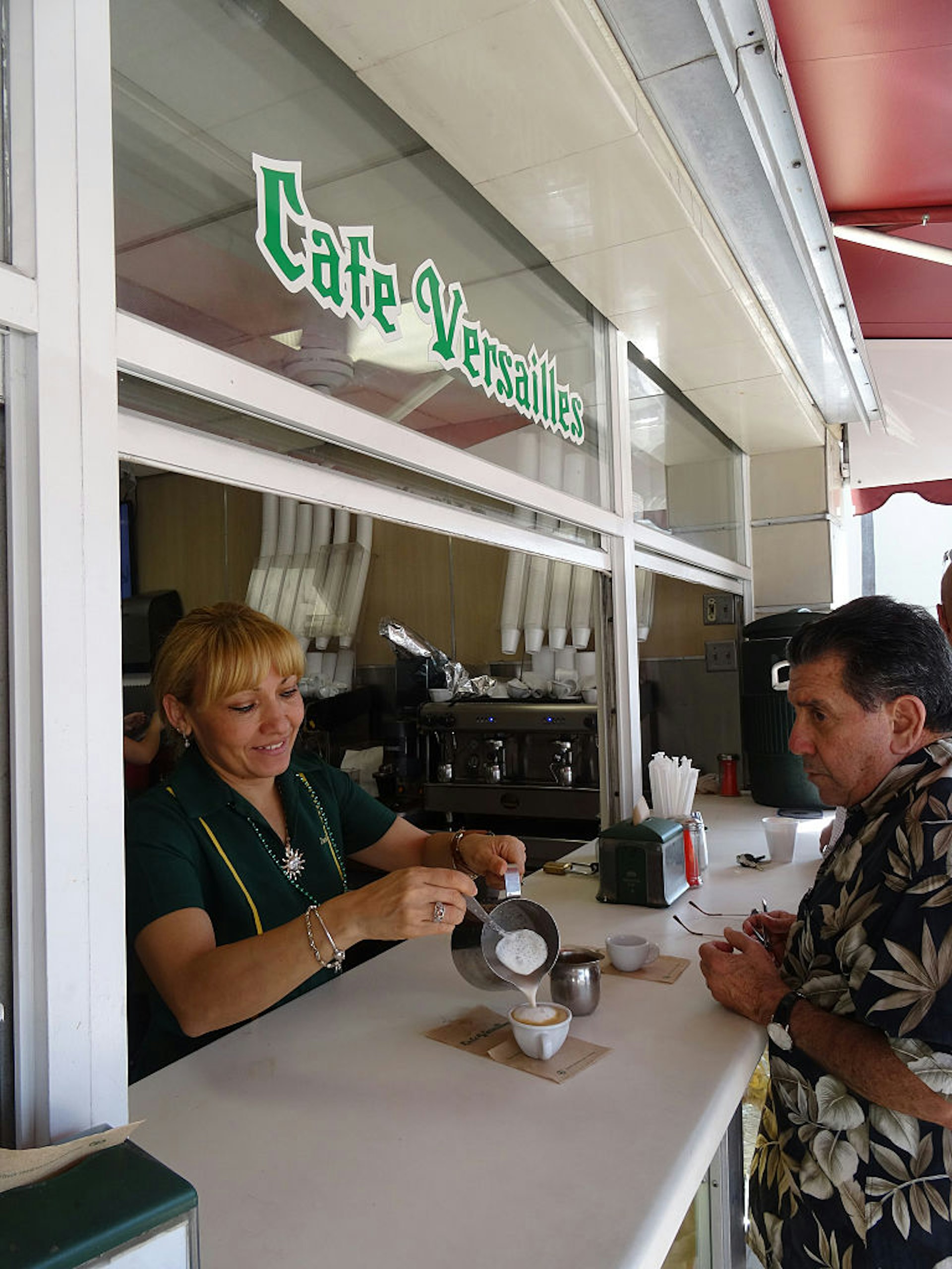 A woman serves coffee to a customer from the ventanita at Café Versailles, Miami