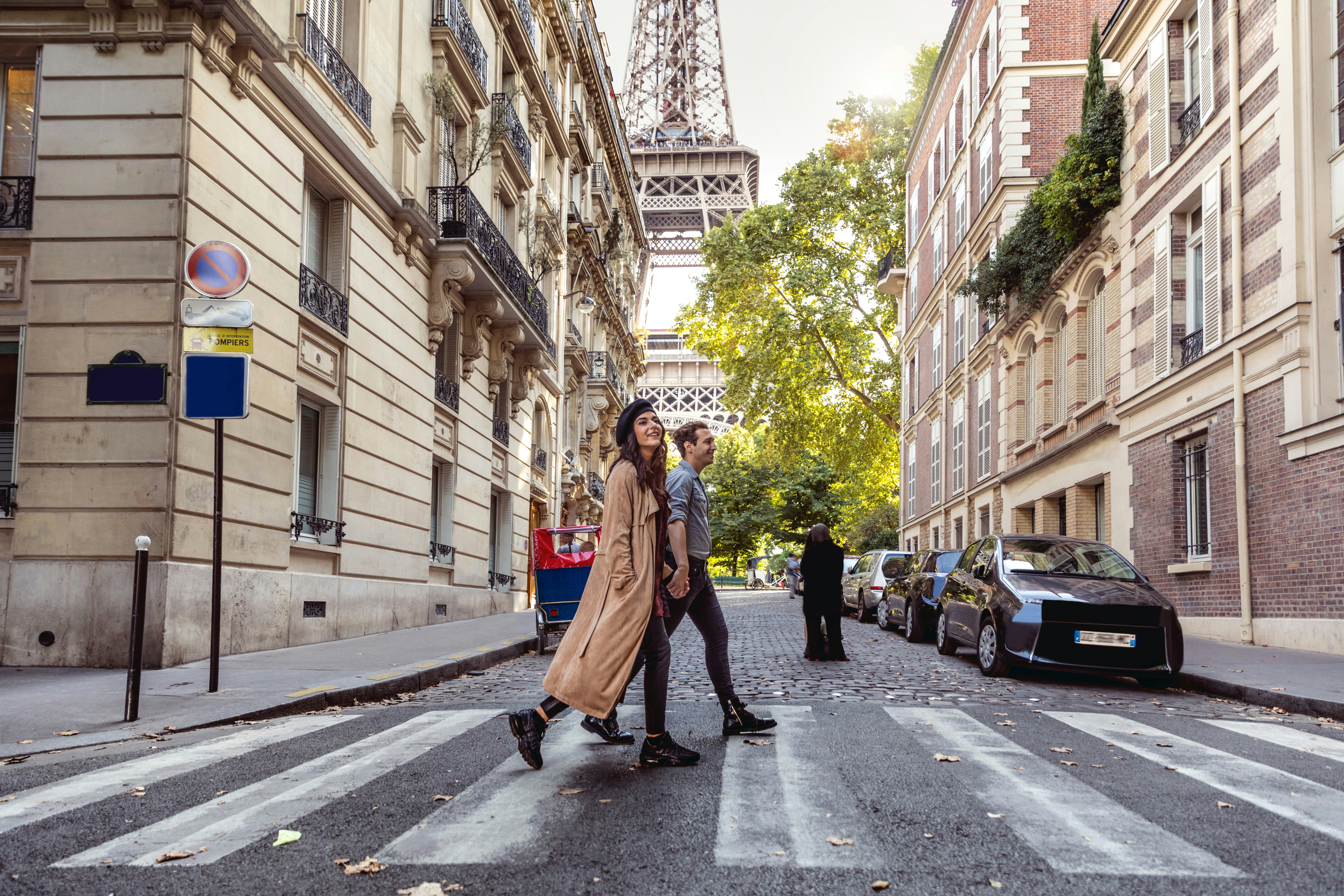 A couple crosses the street in front of the Eiffel Tower in Paris. 