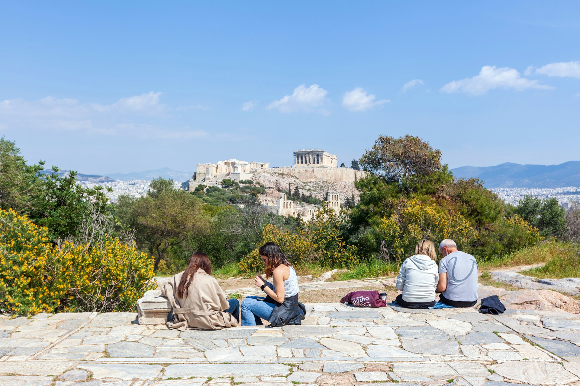 Locals relax in the sun on Filopappou Hill with the Acropolis in the background