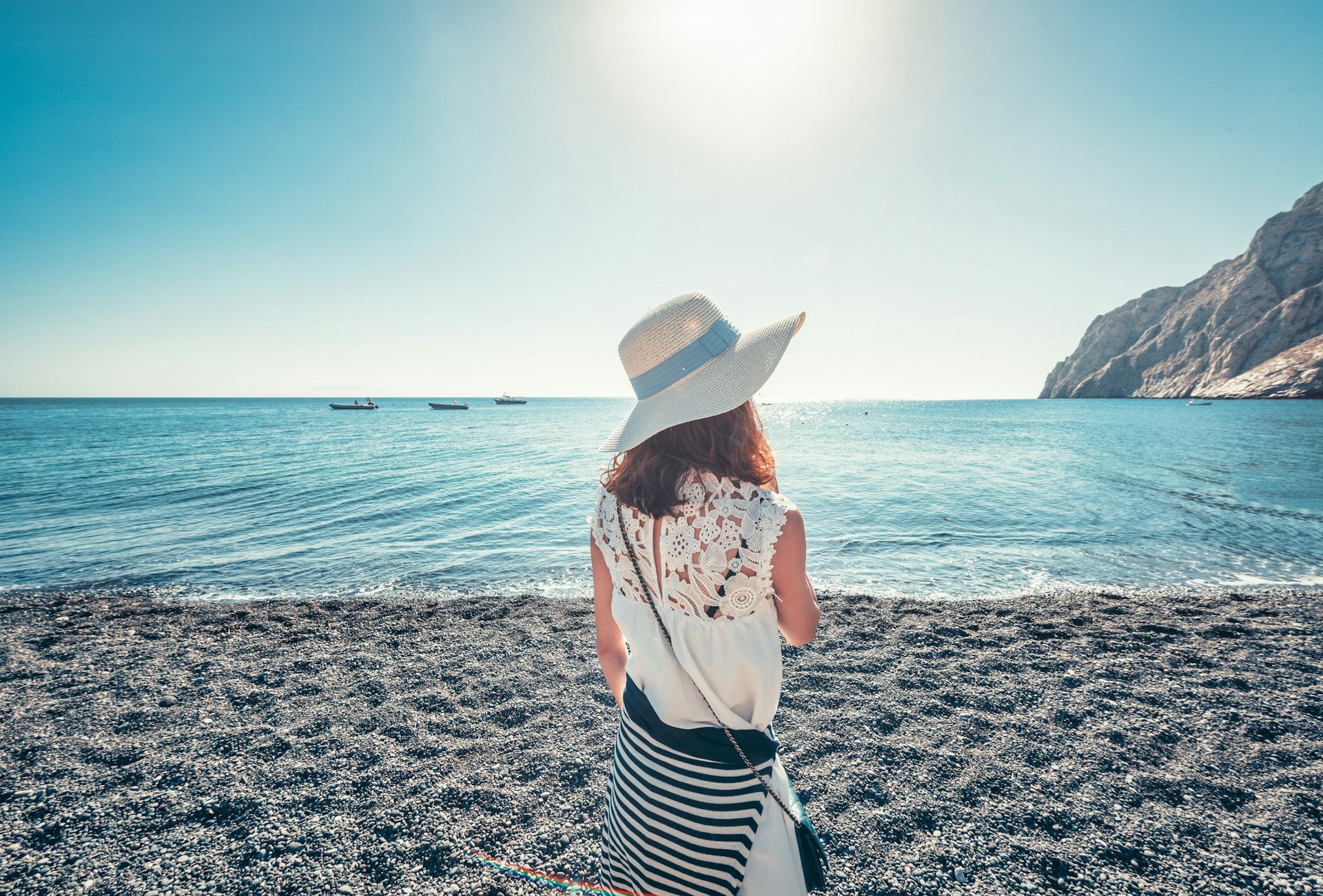 A woman stands alone on the beach and stares out at the sea in Santorini