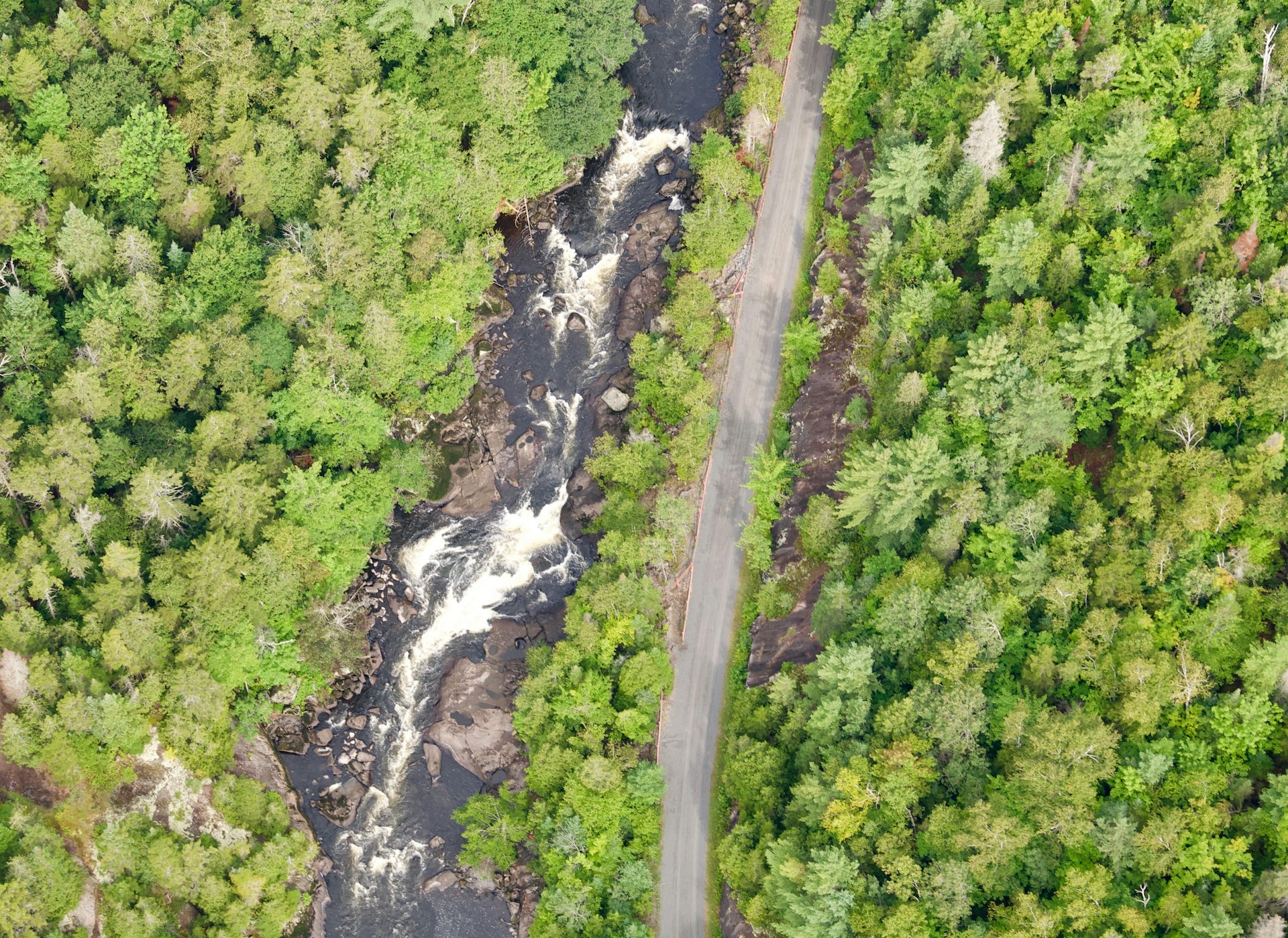 An aerial shot of a bike path running alongside a fast-flowing river surrounded by woodland