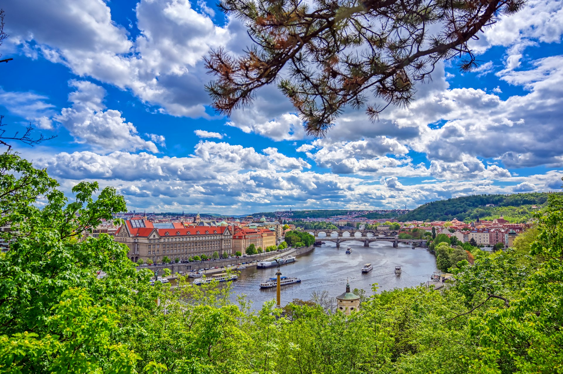A scenic shot of a river flowing through a city center on a sunny day, with perfect white fluffy clouds in a blue sky