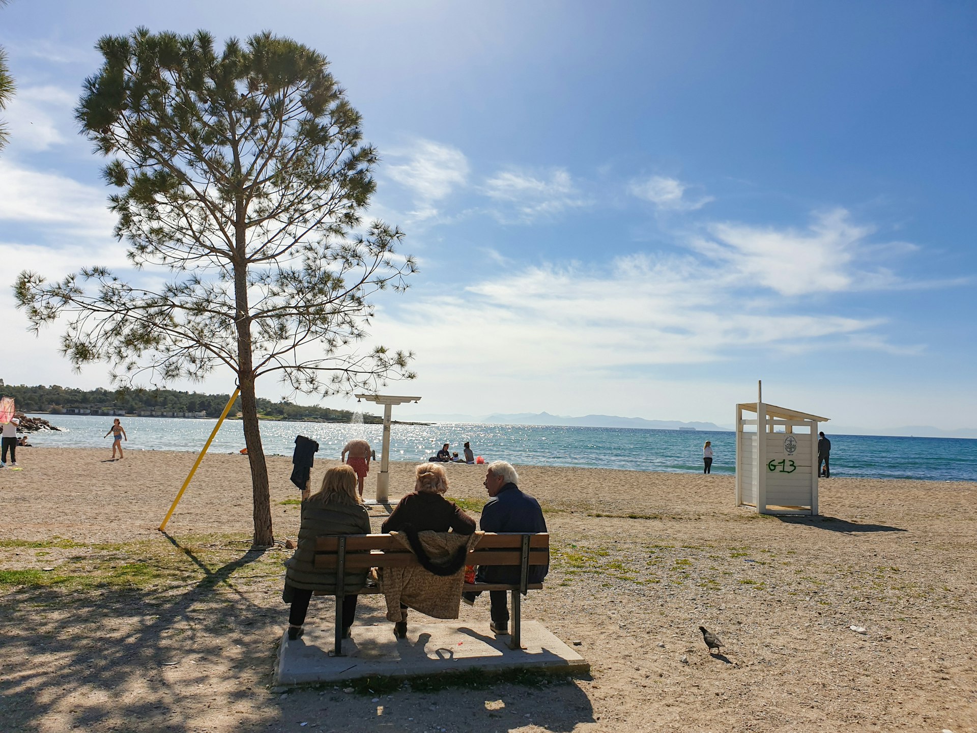 Three people sitting on a bench at the seaside of Glyfada Beach, Athens.