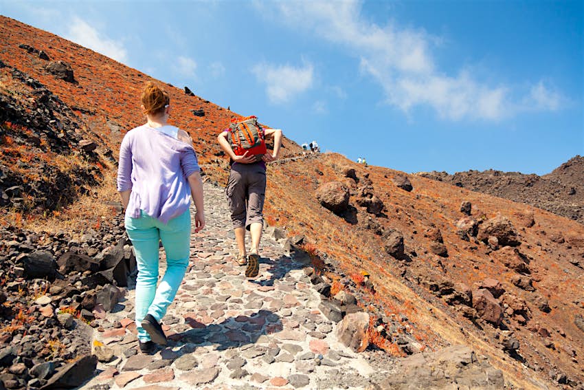 Two people hiking up the black volcanic rock on Nea Kameni