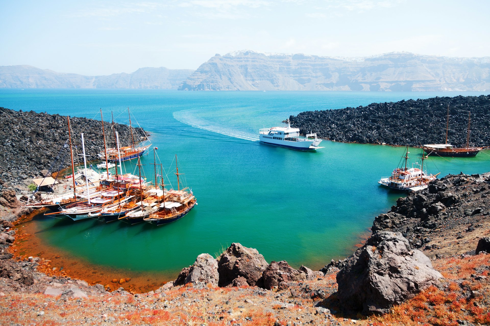 A bay of a volcanic island, with several boats coming into the small harbor