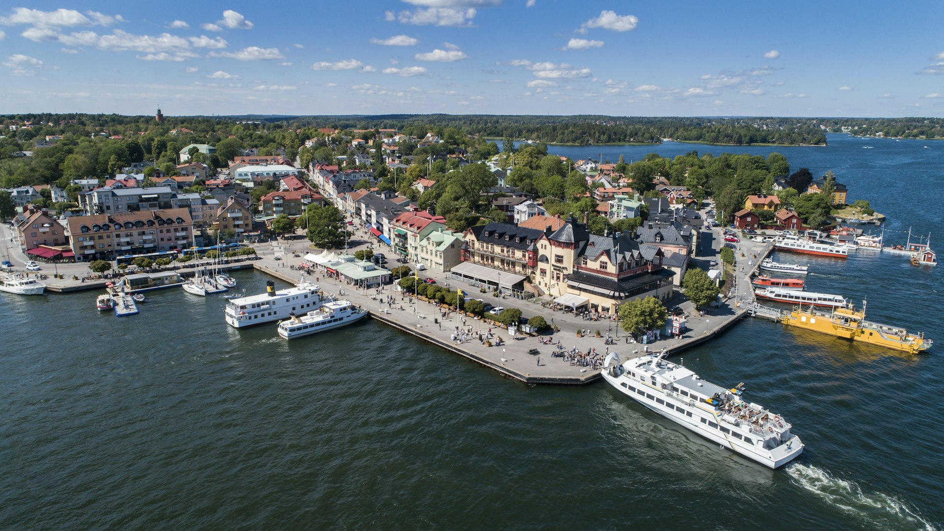 An aerial shot of an island town with colorful buildings and people moving around on a busy harbor-side street