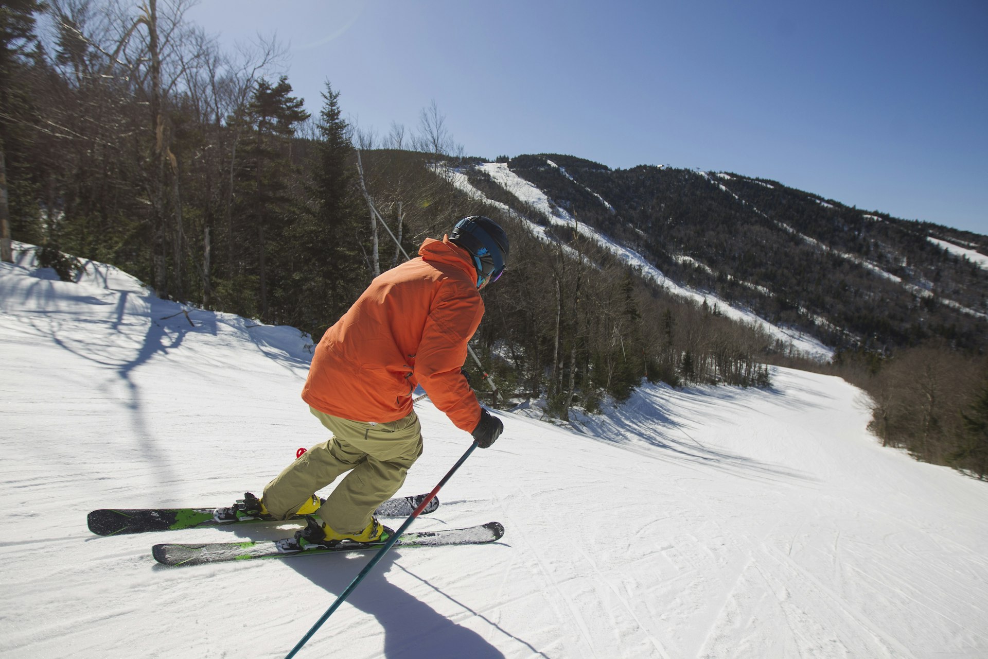 A skiier in a bright orange jacket heads down the snowy slopes