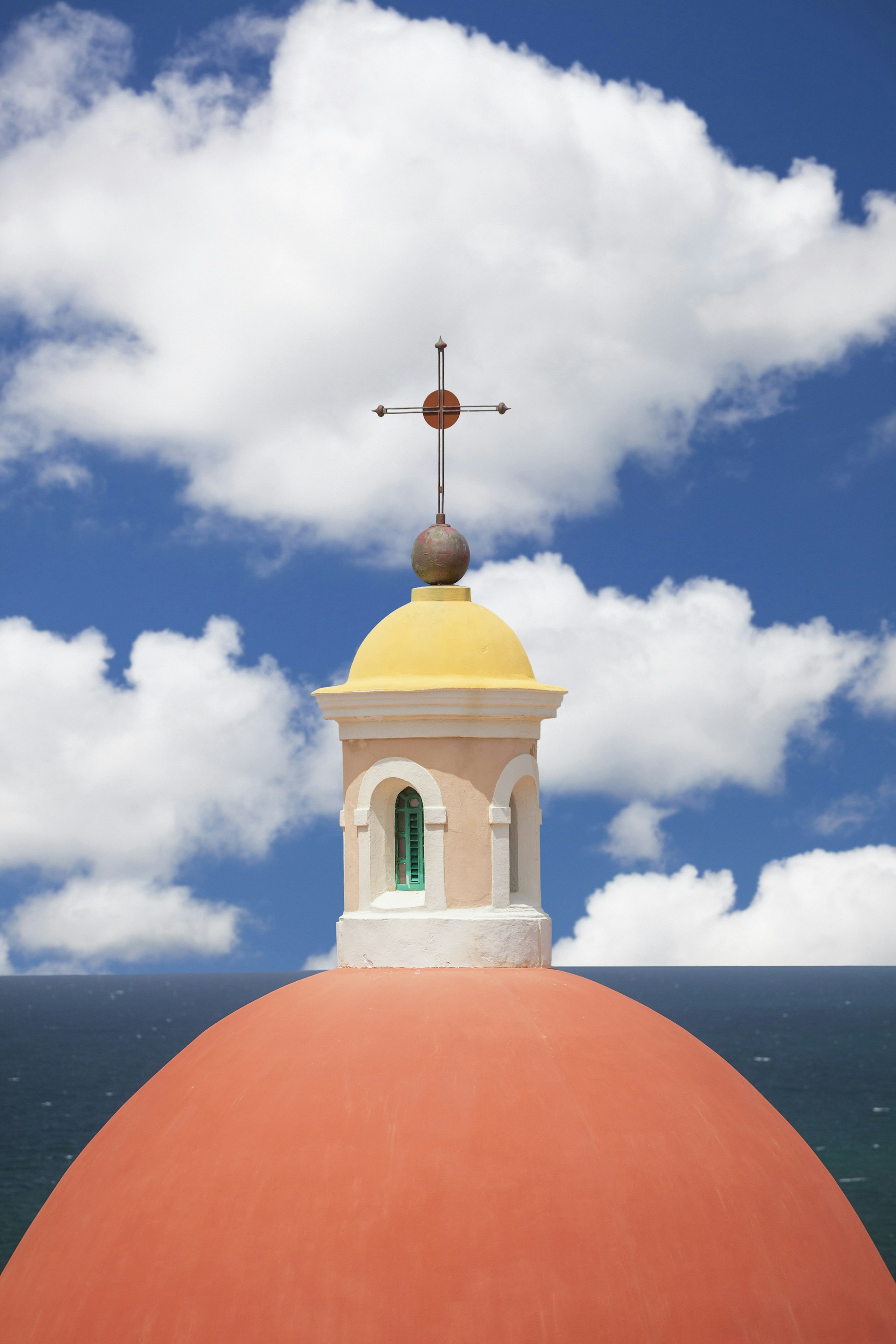 The peach-colored dome of cathedral with puffy clouds in a blue sky in San Juan Puerto Rico