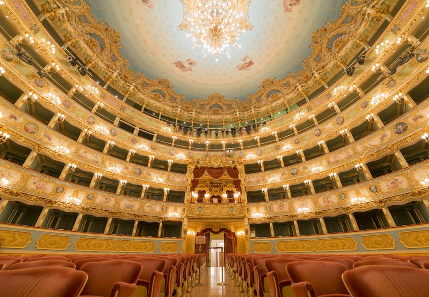 A huge theatre building with red upholstered seats and grand balconies covered in gold decoration