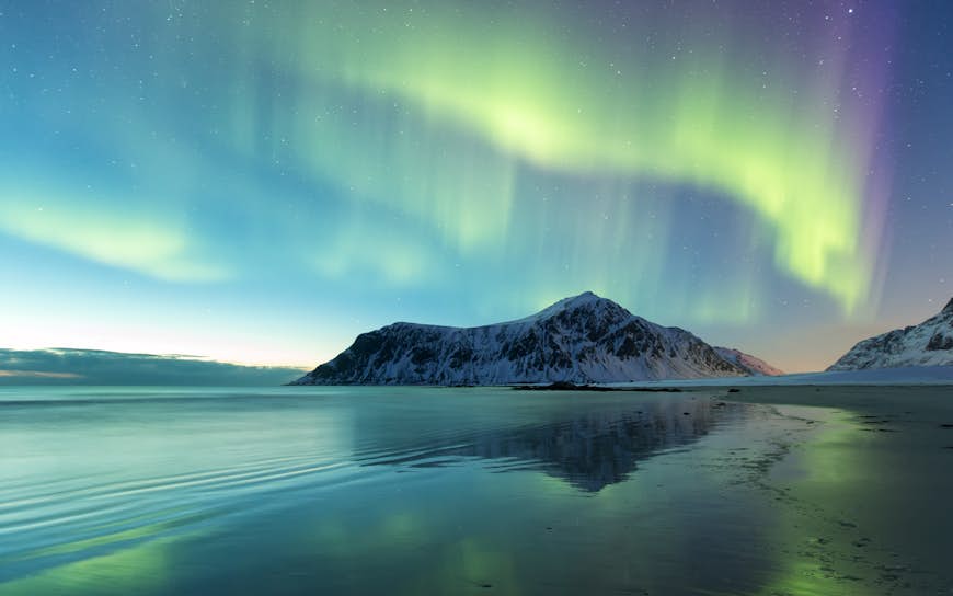 The green and yellow lines of the Northern Lights appear in the sky above Skagsanden Beach, Norway.