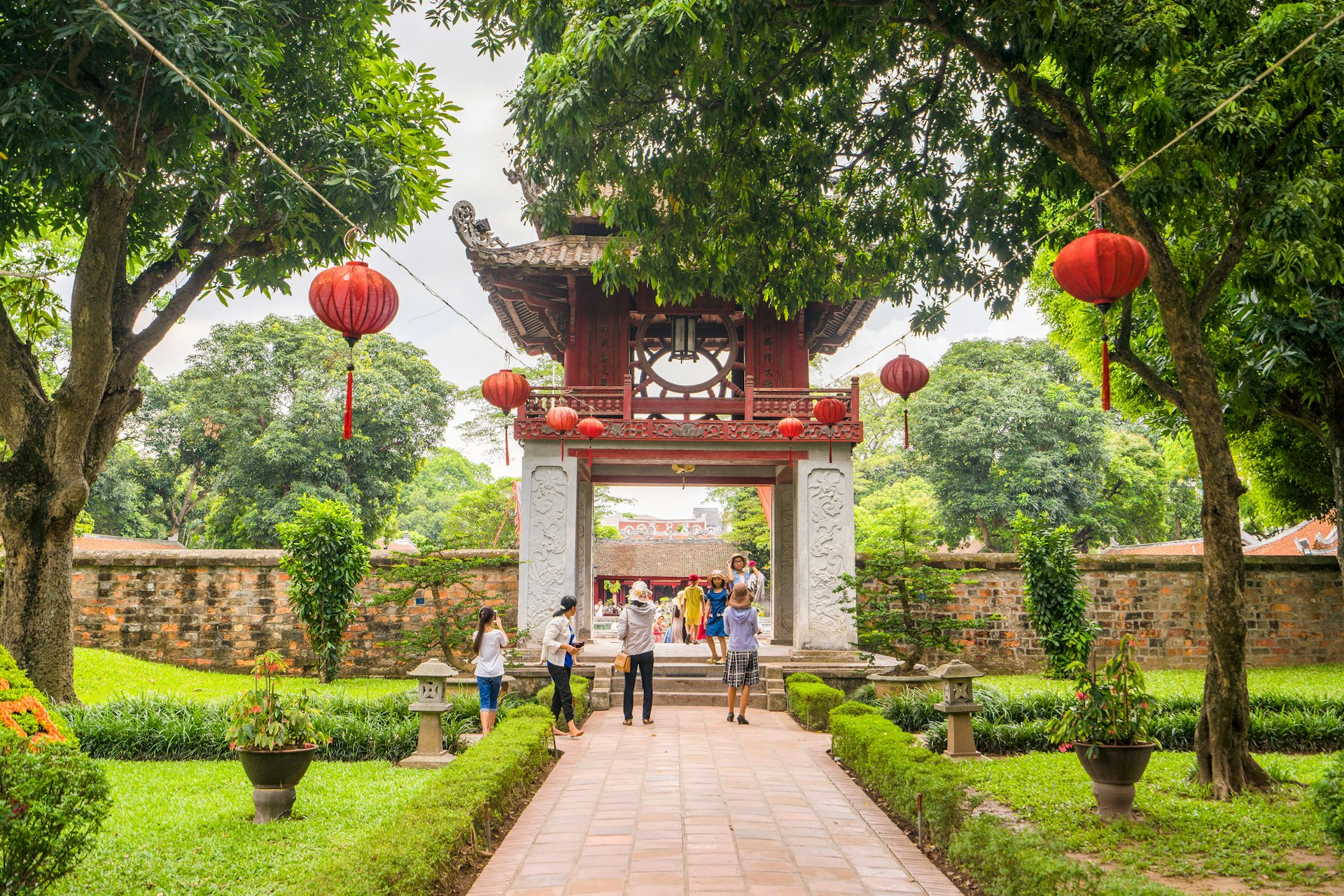A path leads to a huge decorative gateway with a red pagoda-style roof in manicured gardens