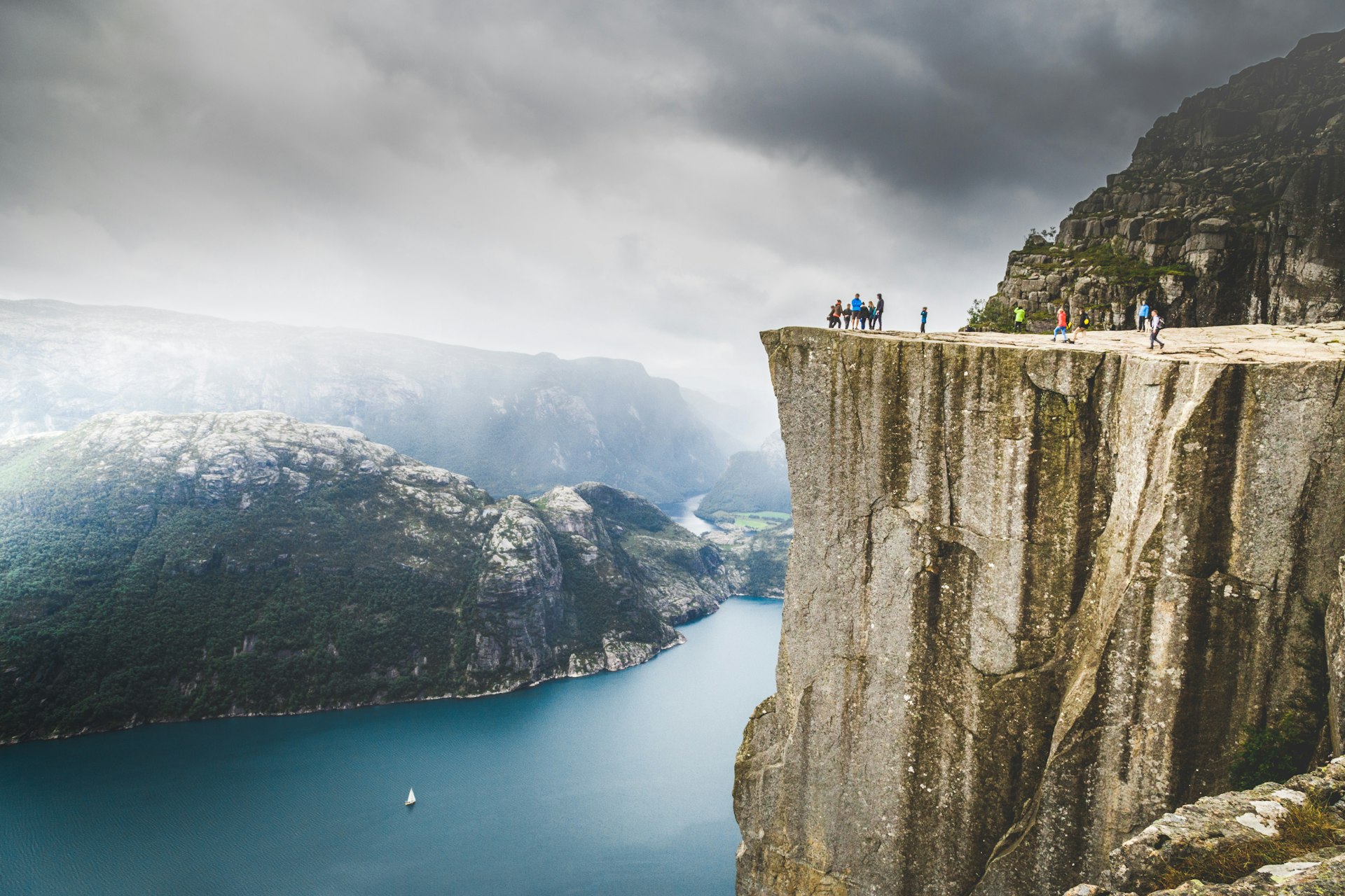 People walking upon Preikestolen, famous nature landmark in Norwey. Lysefjorden and mountains in background.