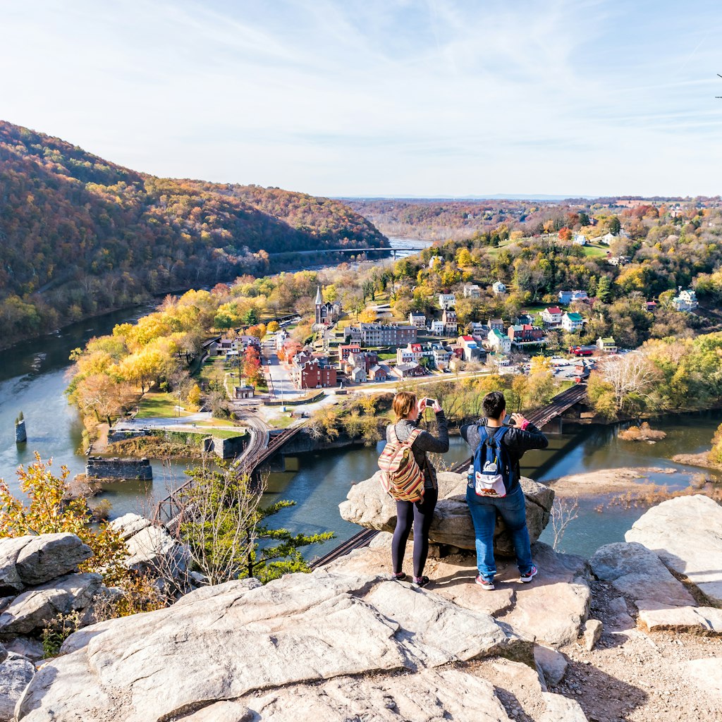 Overlook with hiker people women couple, colorful orange yellow foliage fall autumn forest with small village town by river in West Virginia, WV