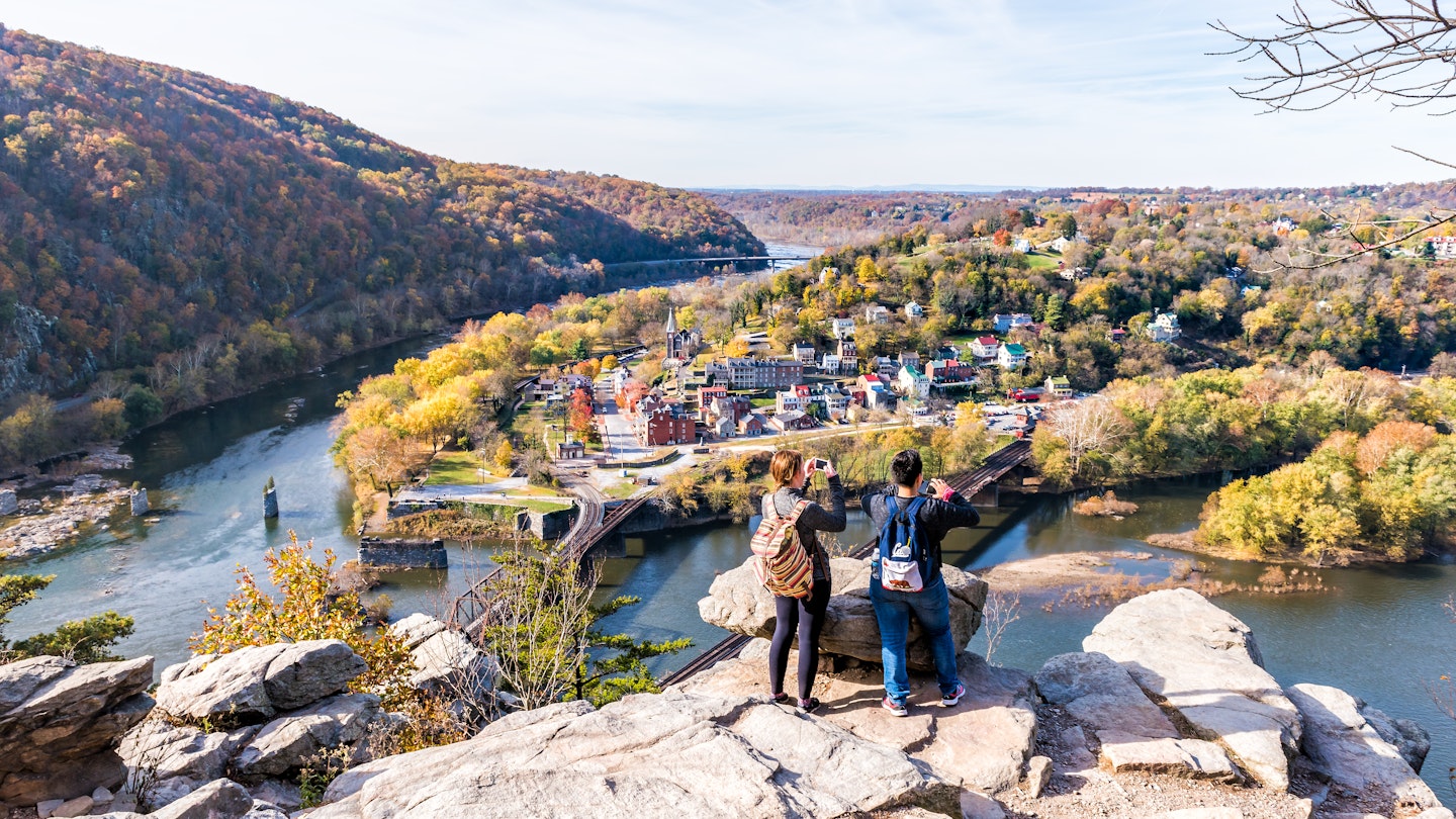 Overlook with hiker people women couple, colorful orange yellow foliage fall autumn forest with small village town by river in West Virginia, WV