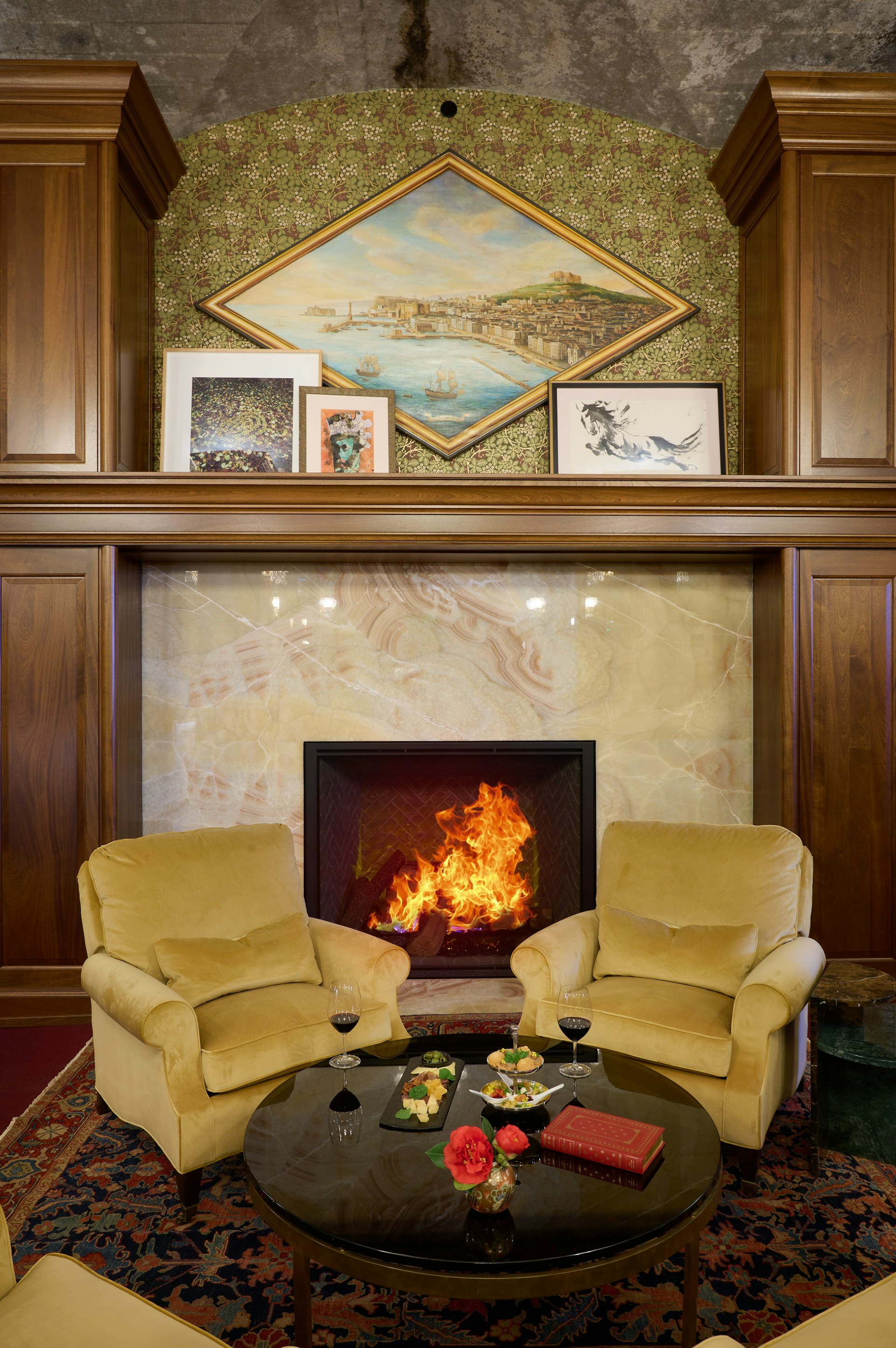 Two leather armchairs in front of a fireplace. There is food and wine on the table.