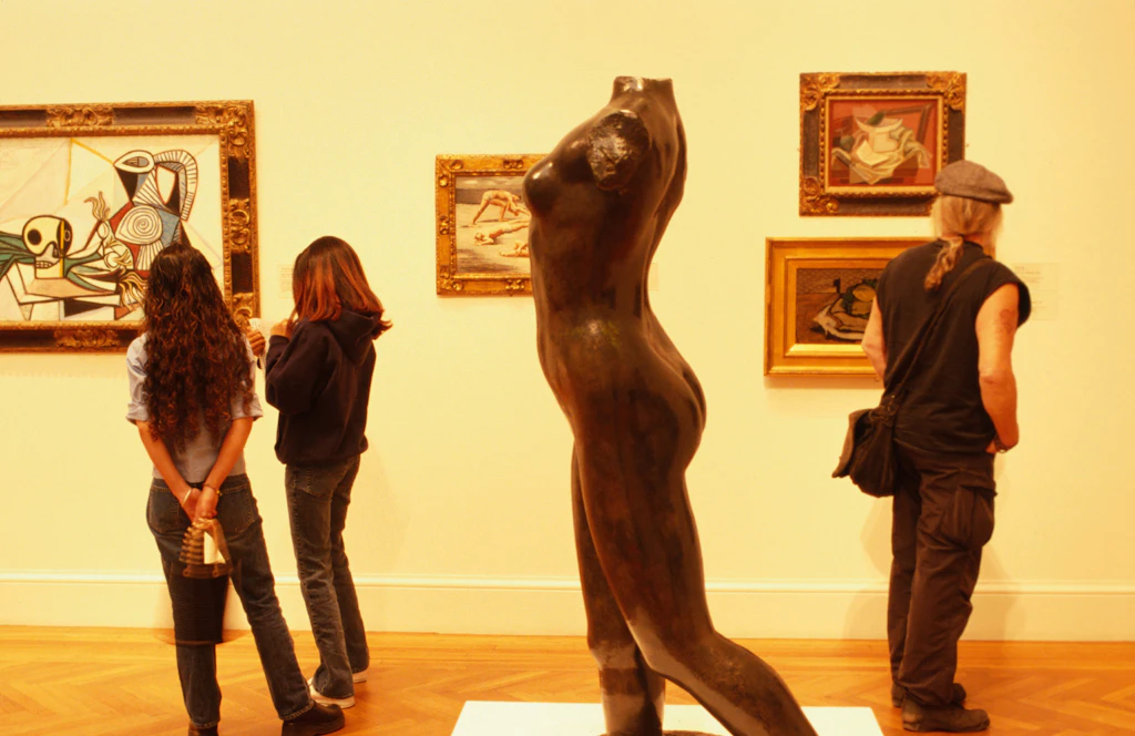 A small group of visitors nose around one of the rooms in the Legion of Honor in San Francisco. Paintings hang on the wall and a sculpture takes up much of the foreground.