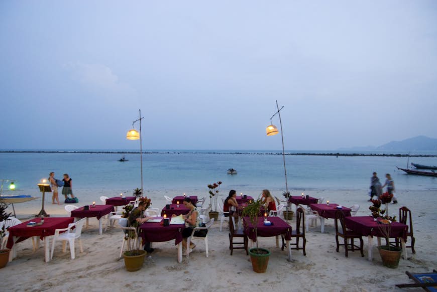 A series of tables and chairs laid out on a beach at dusk awaiting a busy night of diners