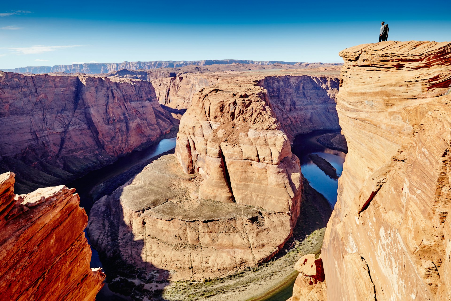 People standing on a cliff overlooking a horseshoe bend in a canyon river