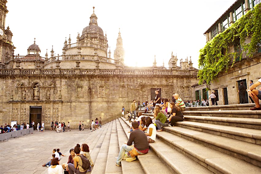 Small groups of people sit on steps with city walls and a large cathedral in the background
