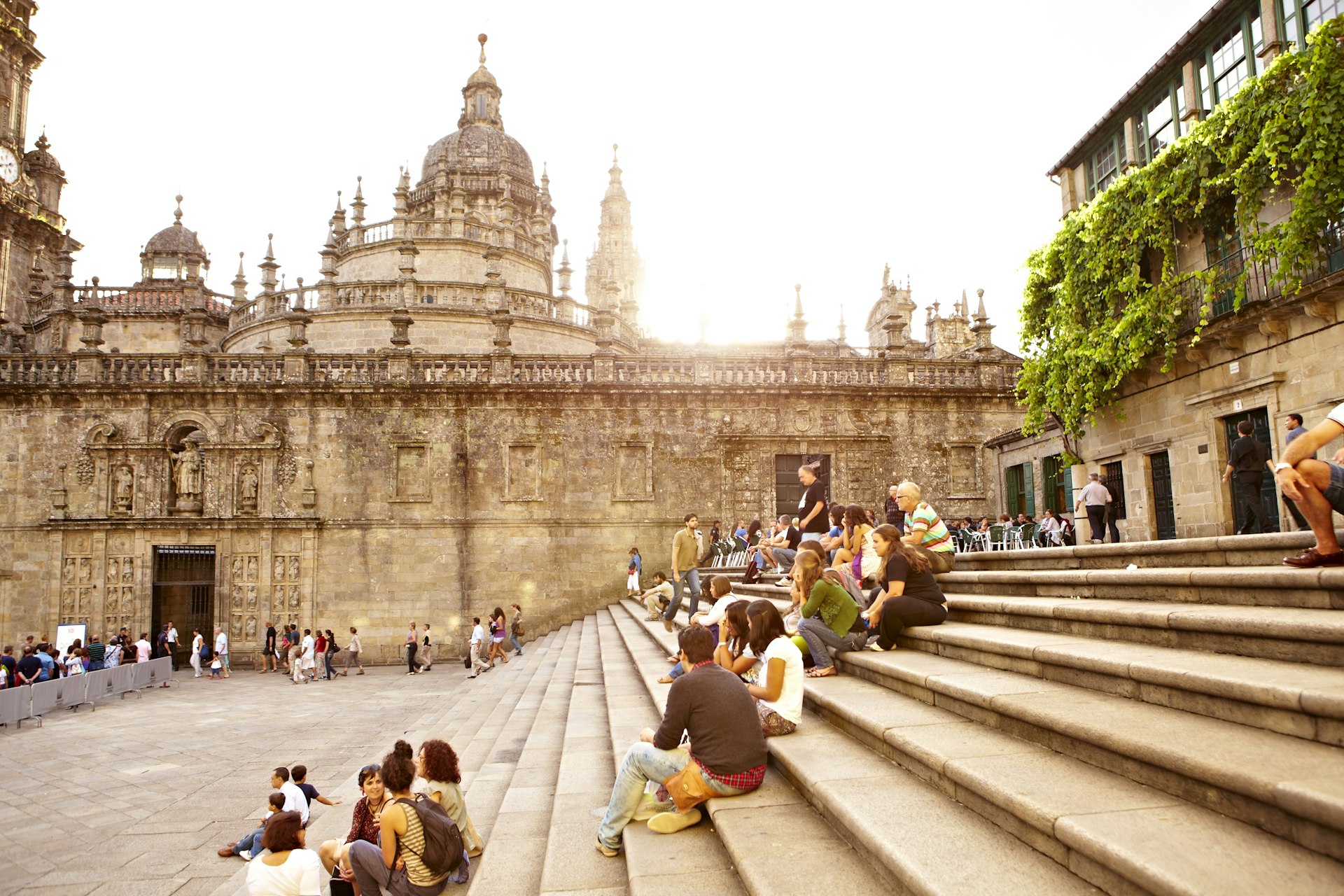 Small groups of people sit on steps with city walls and a large cathedral in the background