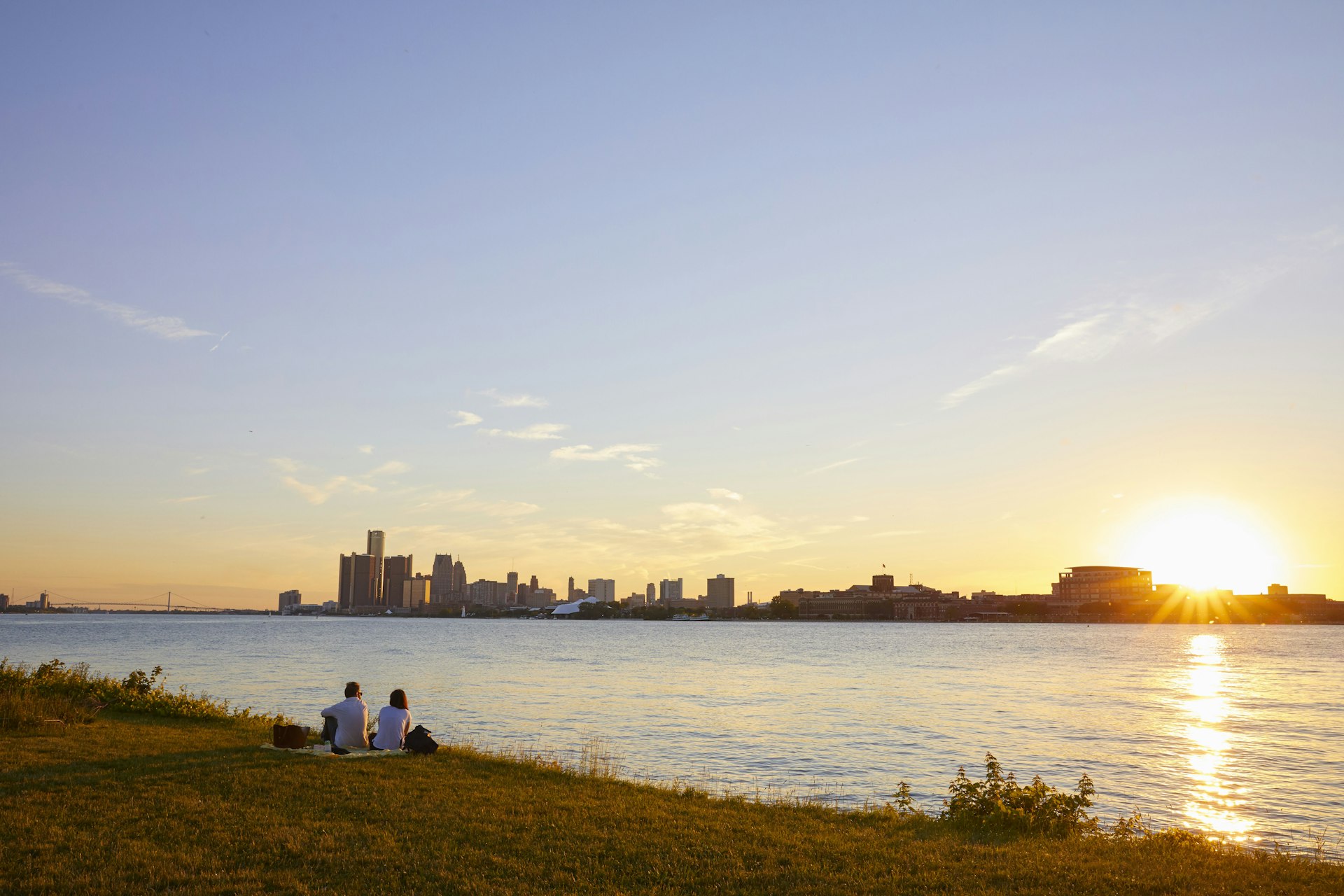 Two people watch the sunset from Belle Isle with the skyline of Detroit in the background