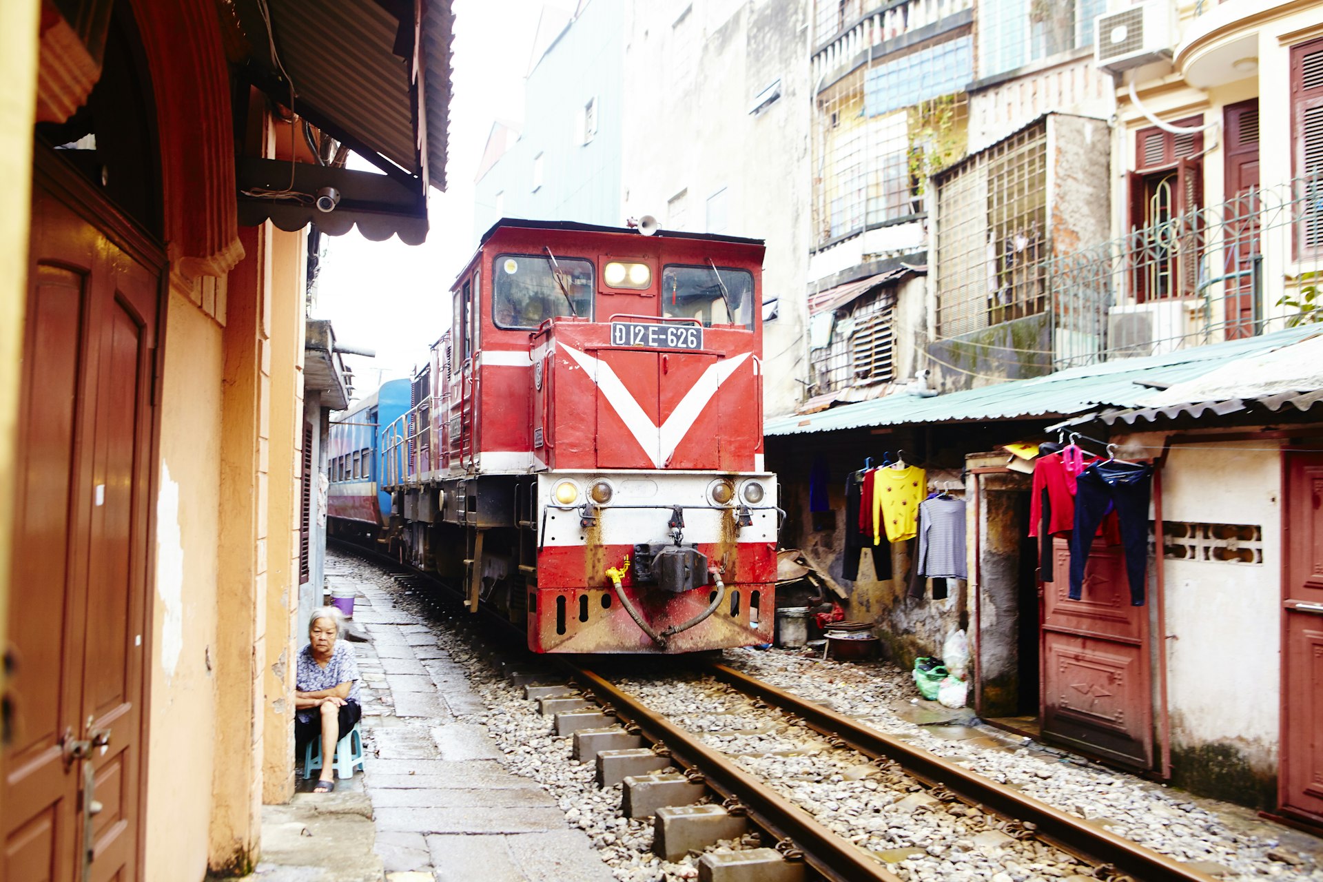 The front of a train engine on the rails that run along a narrow street lined with shop fronts 