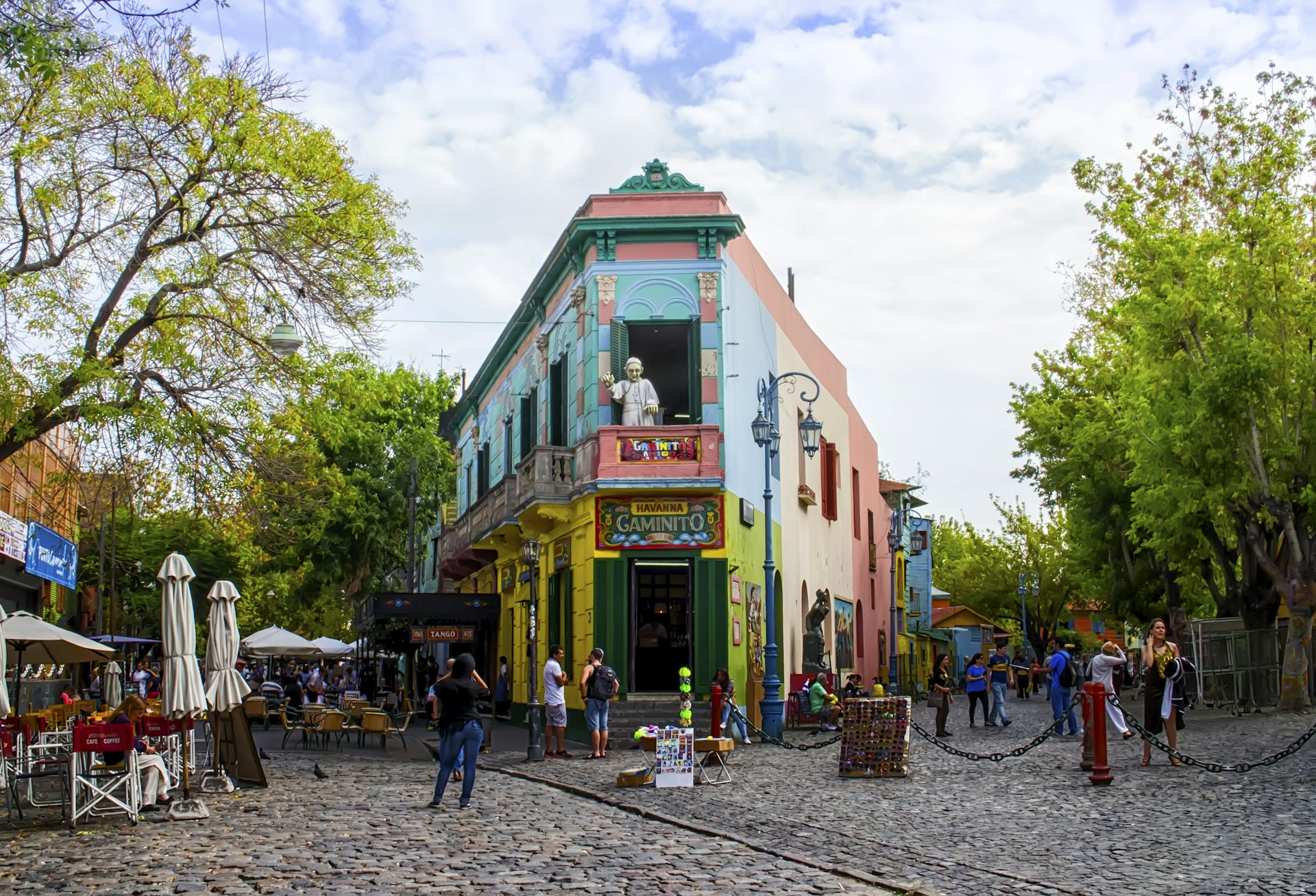 A colorful building dominates a small pedestrian cobbled street lined with stalls and cafes