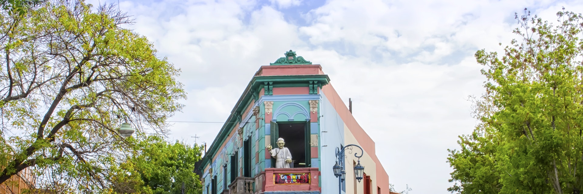 Buenos Aires, Argentina - April 15, 2015: The main square on of the Camanito in the La Boca neighborhood of Buenos Aires features brightly colored buildings and cobblestone streets that are a popular tourist destination. Tourists can be seen surrounding the most recognizable building the the neighborhood at the center of the square. The area is a popular destination for watching tango dancers in the street, shopping for souvenirs handicrafts made by local artisans and restaurants. It is the oldest neighborhood in Buenos Aires and is located at the mouth of the port, which gives it its namesake.