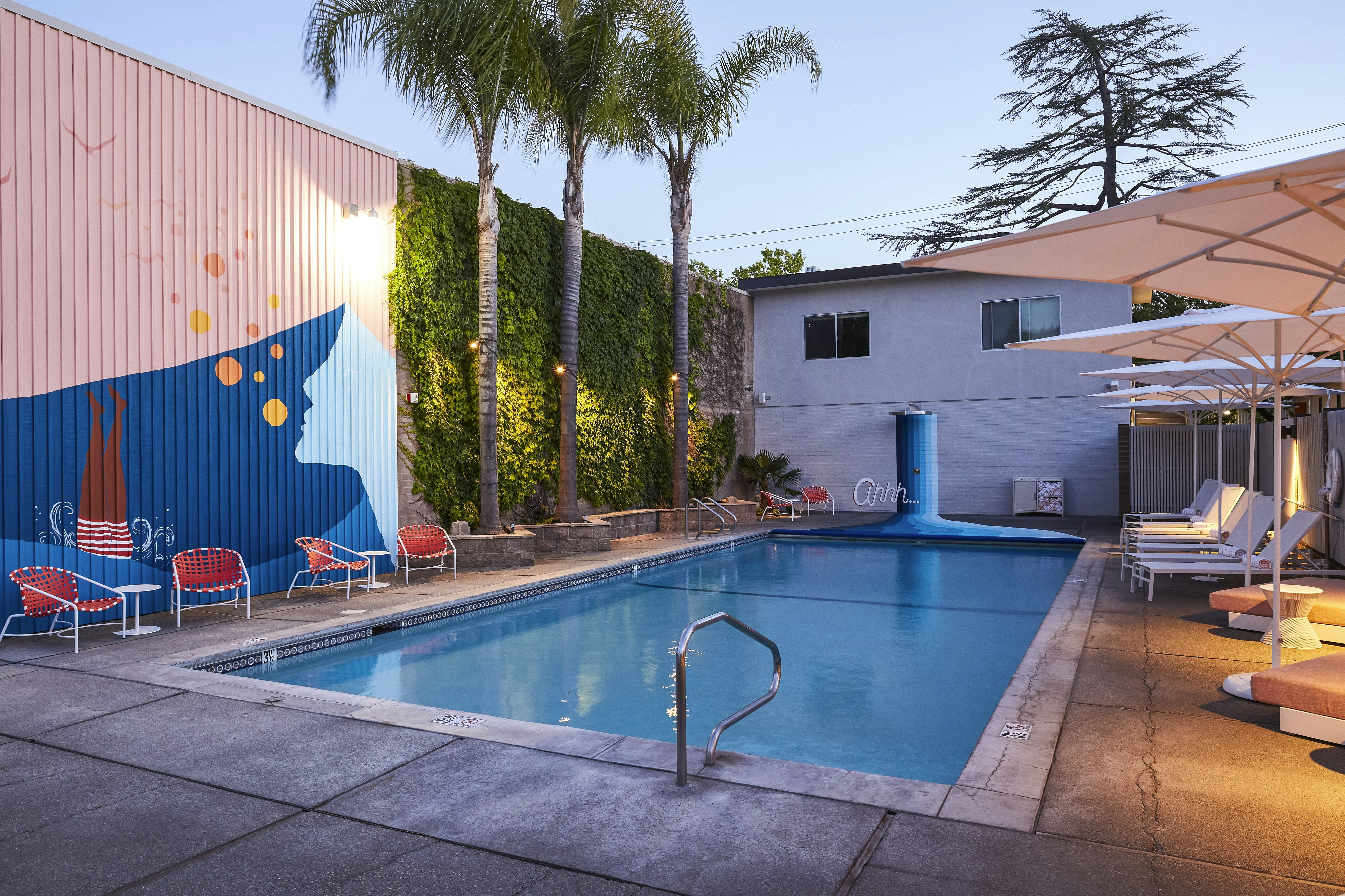 A shot of an outdoor swimming pool in the evening. There are colorful murals on the walls surrounding the pool 