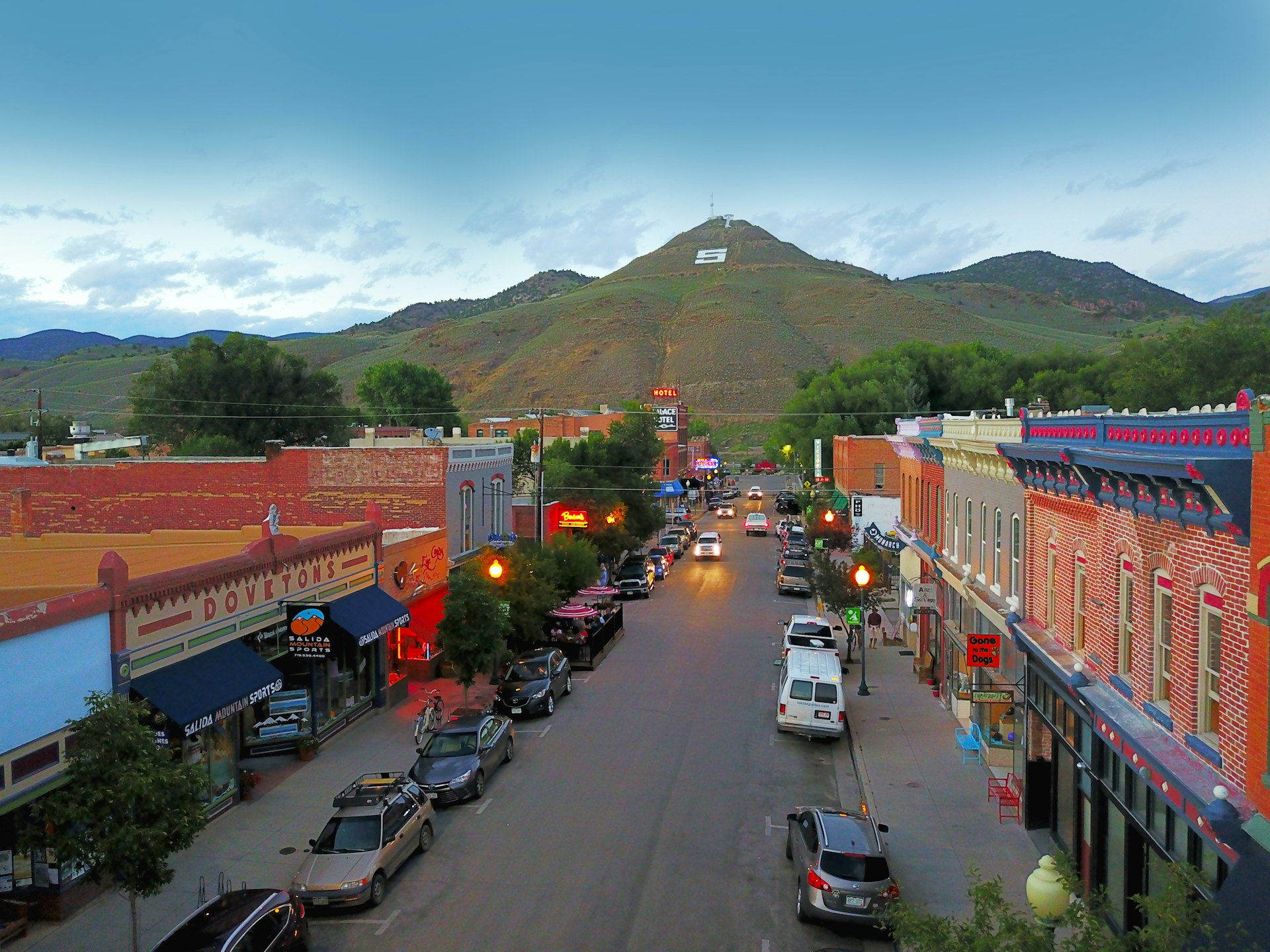 An aerial view of downtown Salida, Colorado, with colorful buildings lining the streets and a mountain with a white S on its slope in the background