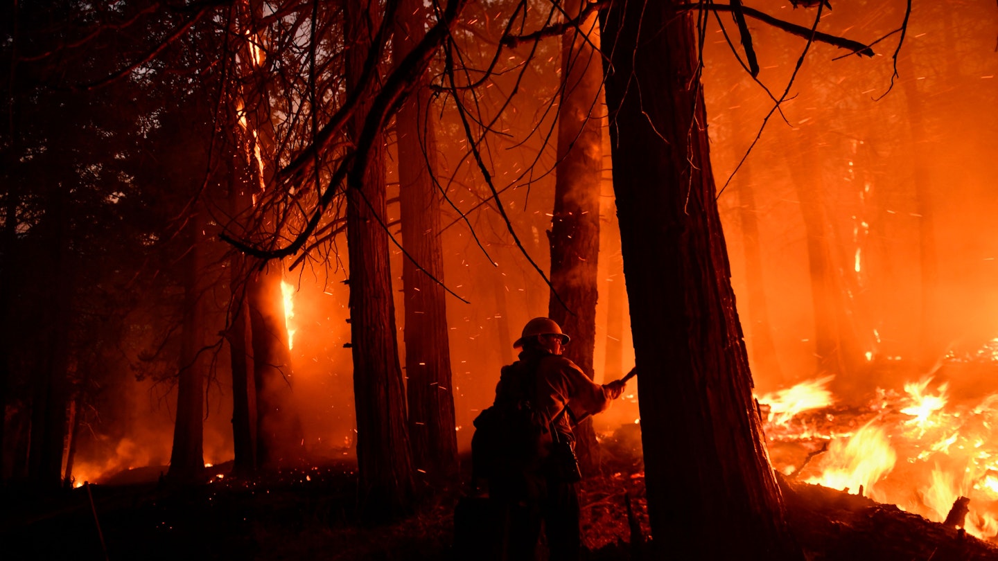 A Kern County firefighter uses a hand tool to keep the fire from spreading as trees burn at night during the French Fire in the Sequoia National Forest near Wofford Heights, California on August 25, 2021. - The wildfire west of Lake Isabella in Kern County has burned over 20,000 acres while threatening homes in and around Wofford Heights and Kernville. (Photo by Patrick T. FALLON / AFP) (Photo by PATRICK T. FALLON/AFP via Getty Images)