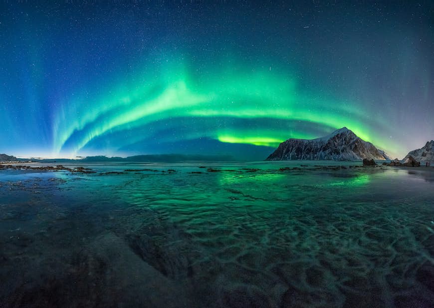 The green lights of the Aurora Borealis light up the night sky above Skagsanden Beach, Norway.