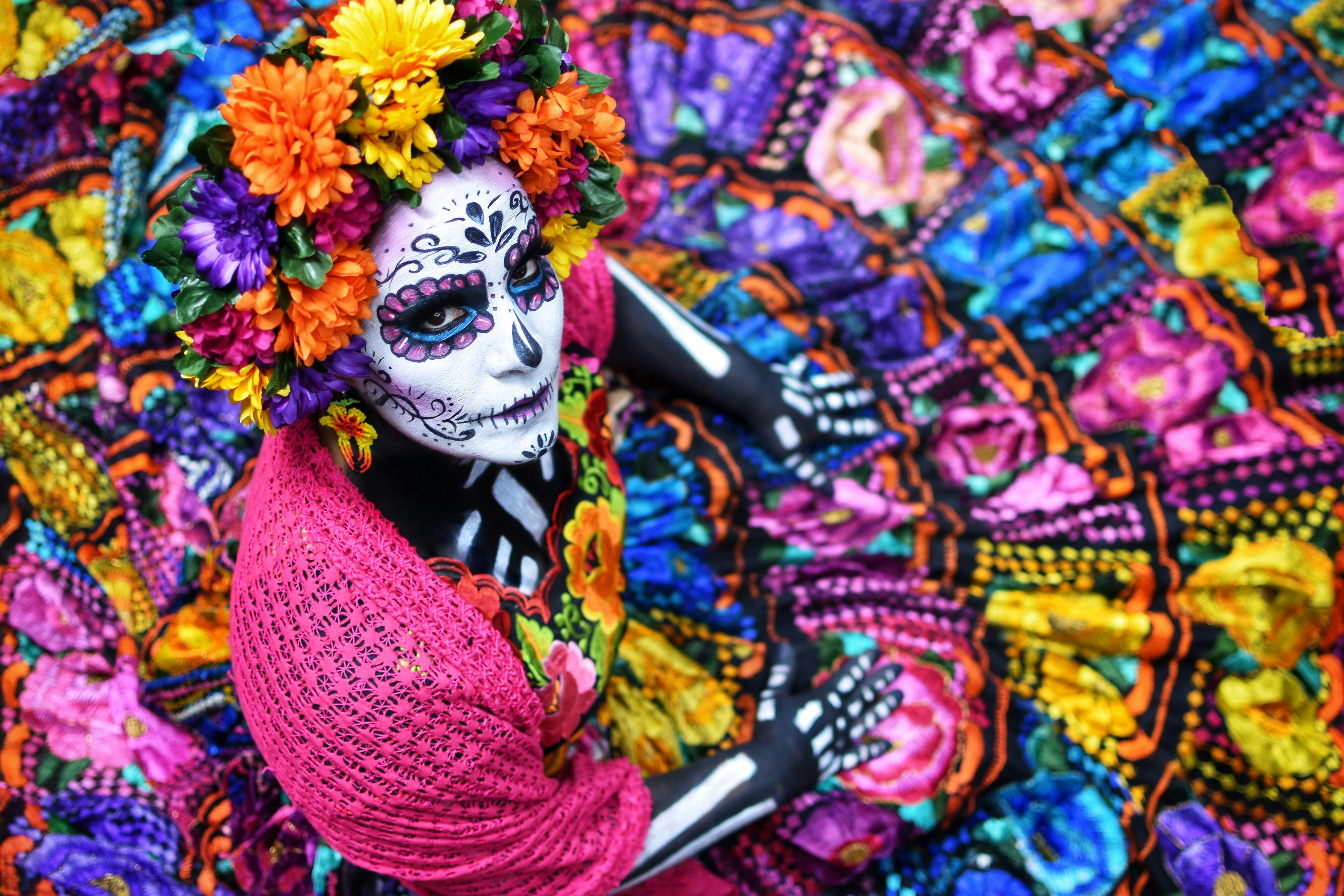 A woman dressed as a Catrina with a white-painted face with black flower patterns, and a flower-covered headdress
