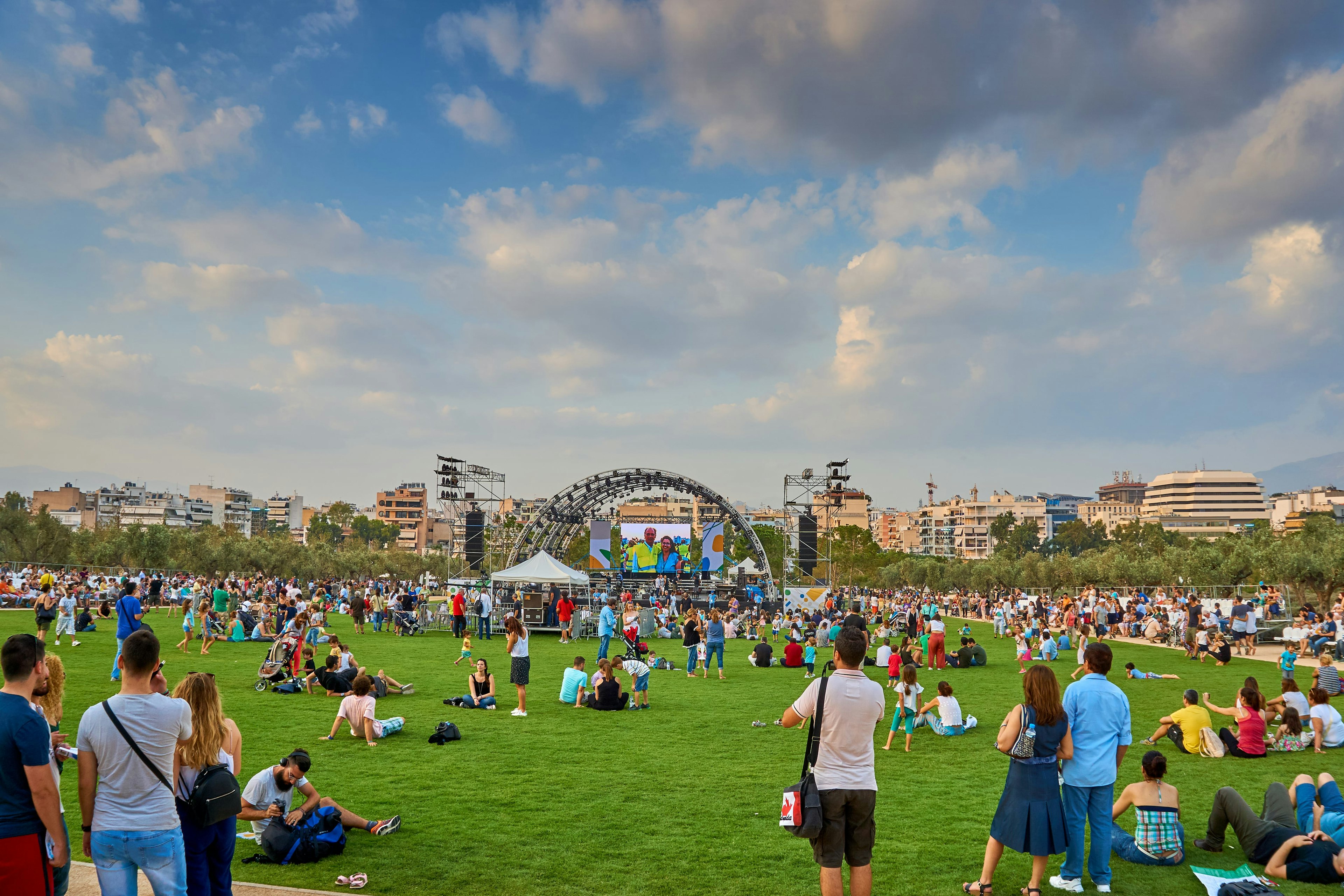 Crowds of people sitting on the grass at Stavros Niarchos Park enjoying a concert in the sunshine