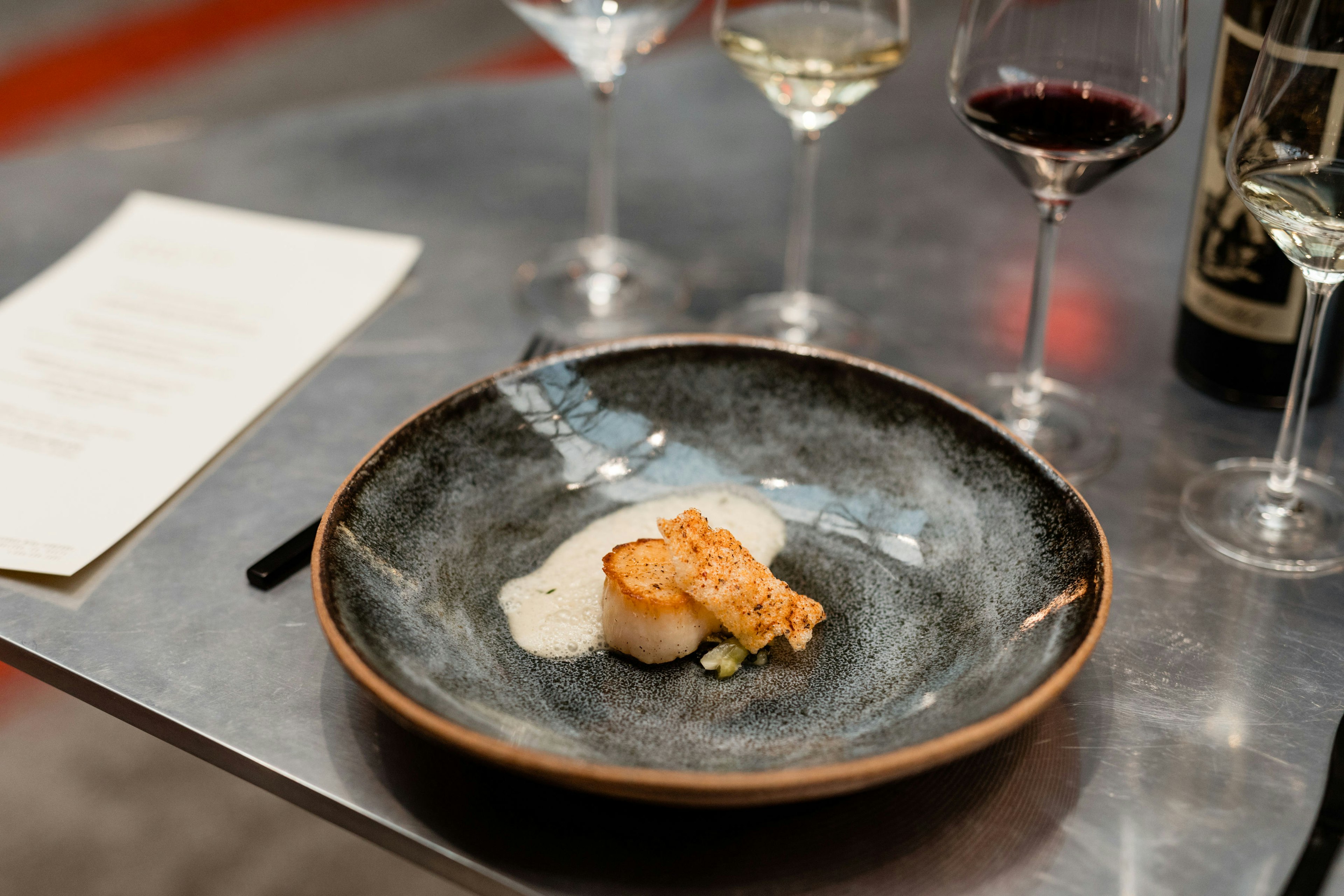 A small dark bowl with a tiny portion of food in it, and two wine glasses