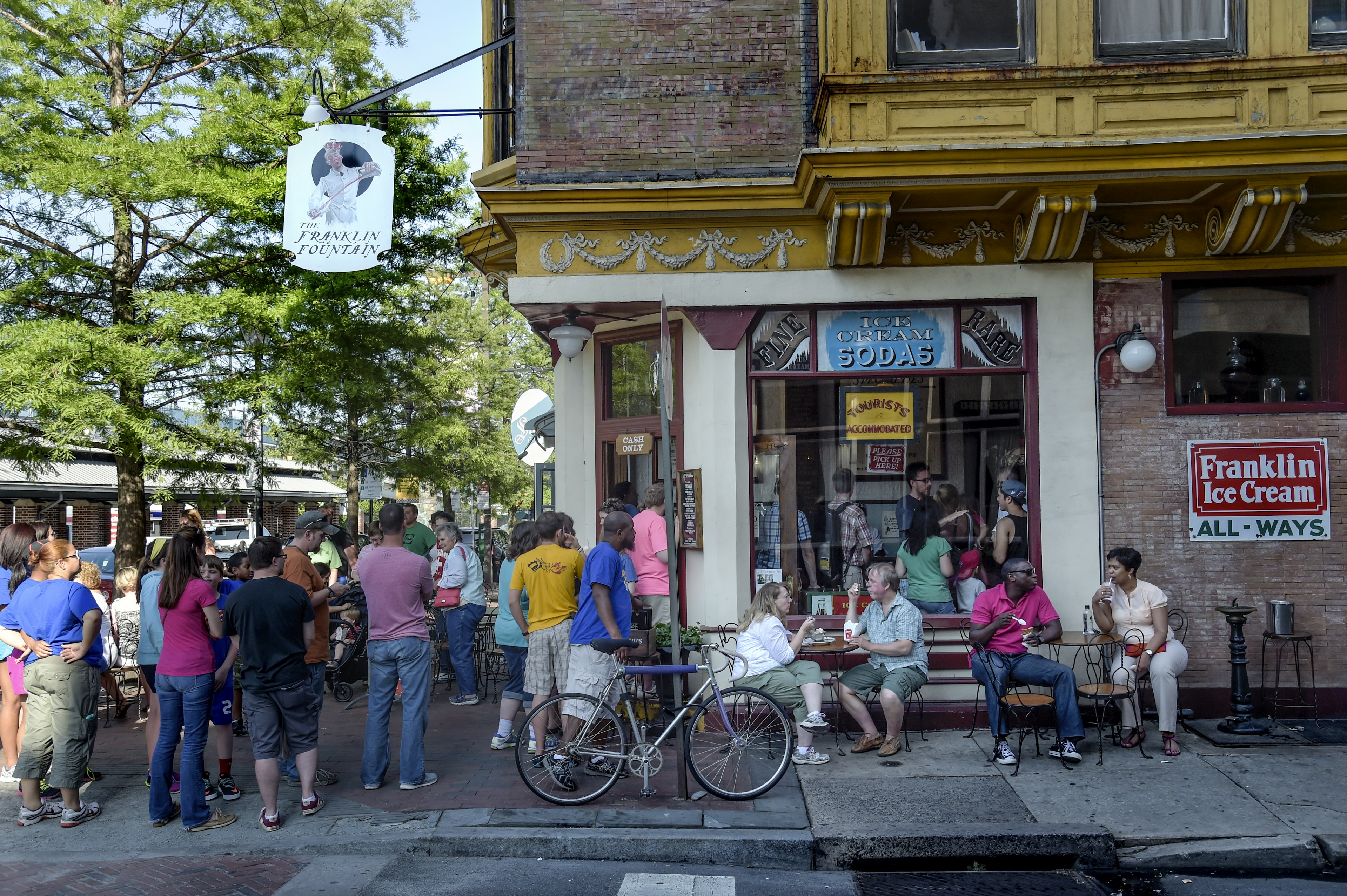 A large crowd stands outside the popular Franklin Fountain, a local ice cream shop in Philadelphia.