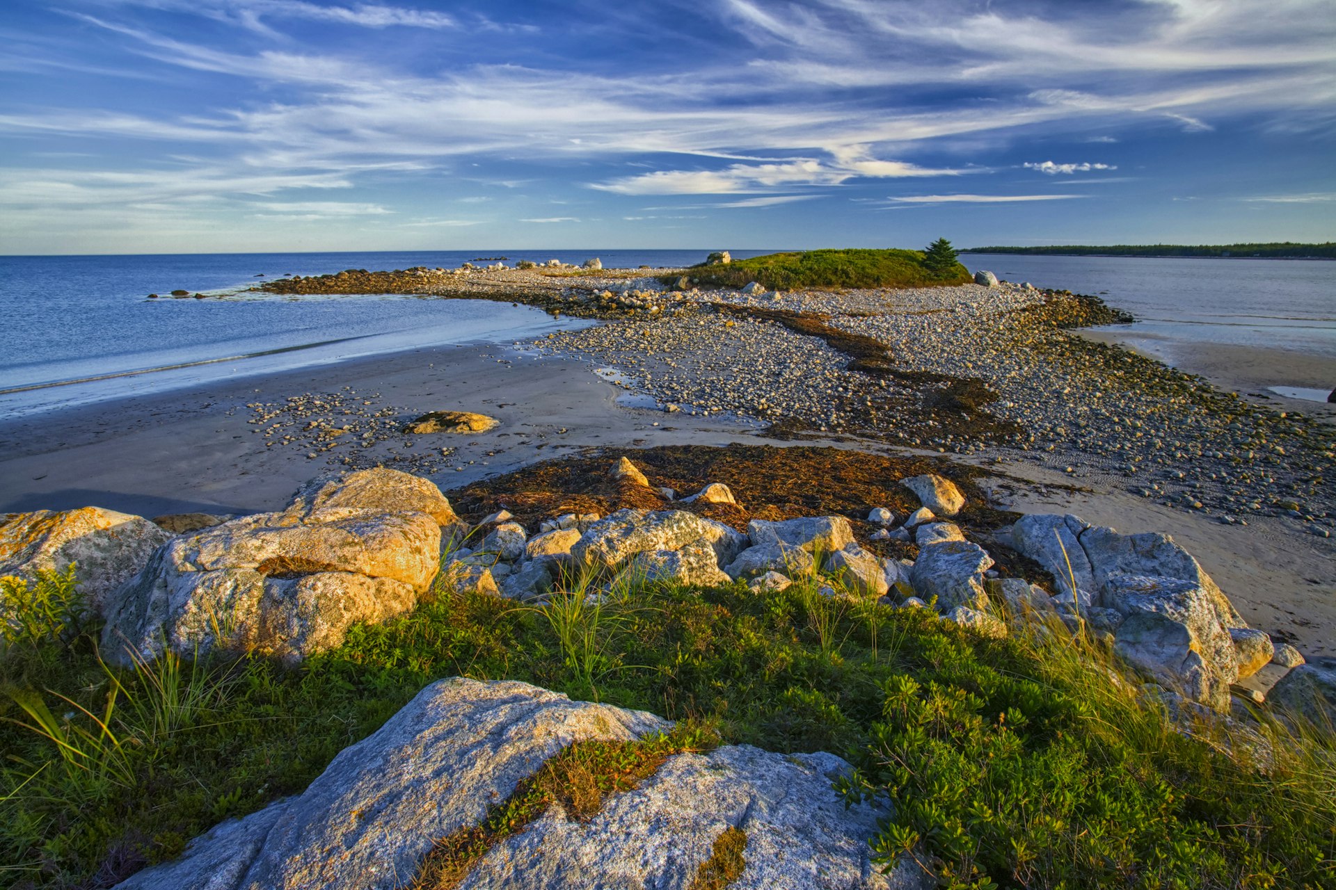 A rocky coast with a small peninsula jutting out into calm waters, with blue skies above