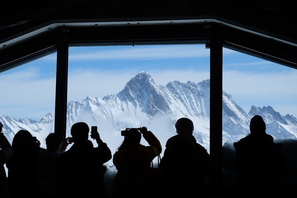 Silhouette People Looking At Snowcapped Mountain Through Window Silhouettes of tourists look out through a giant window at the snowy mountainous landscape surrounding Jungfraujoch.