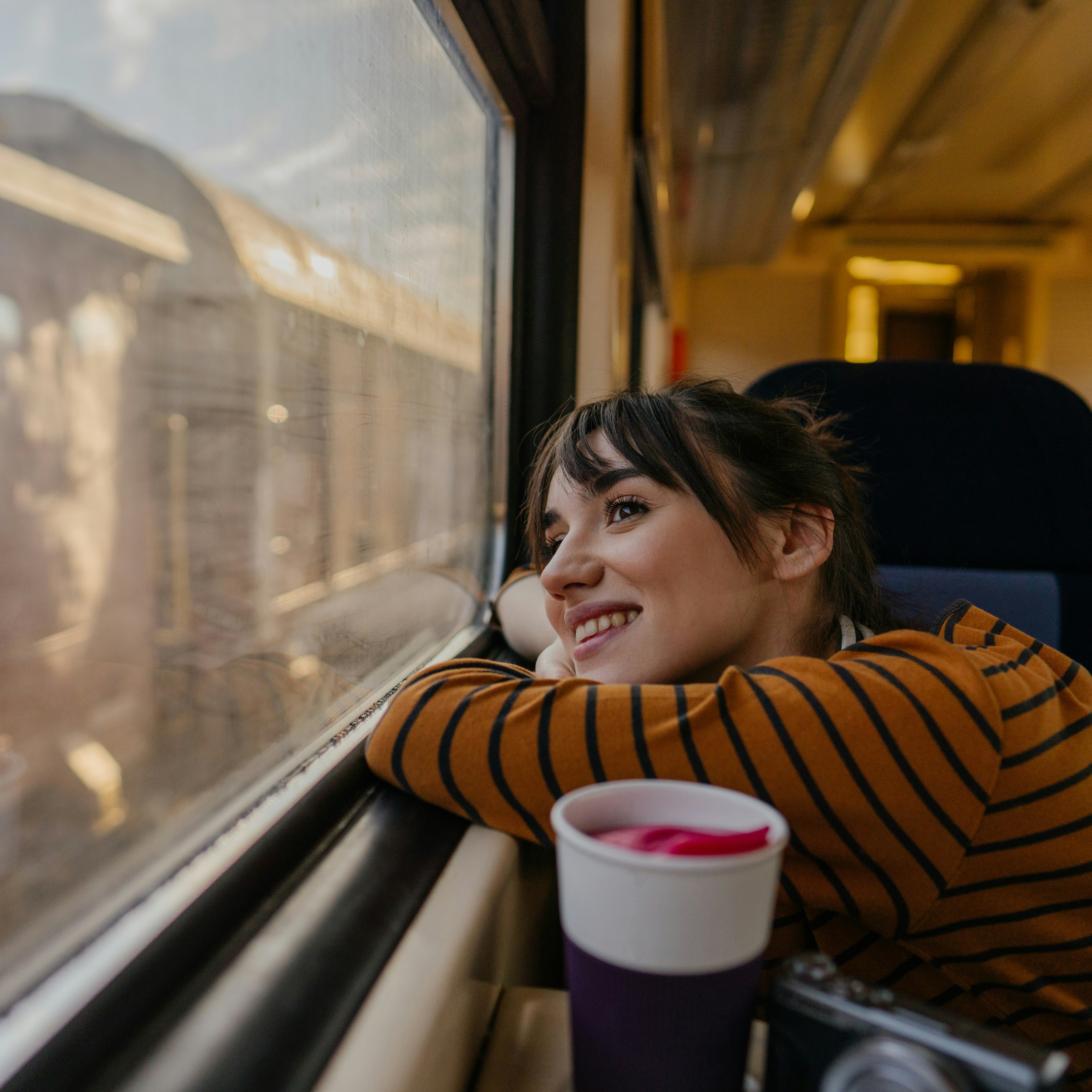 Photo of a young woman riding on a train, enjoying her trip while looking through the window