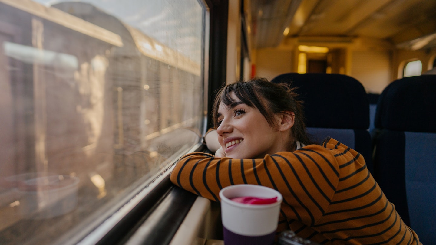 Photo of a young woman riding on a train, enjoying her trip while looking through the window