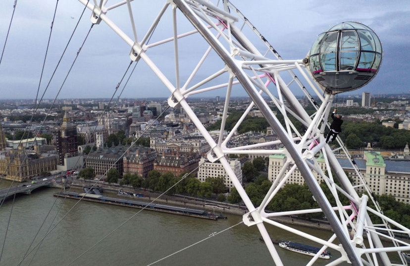 A man dressed as Britain's most famous secret service agent, James Bond, is silhouetted against the London skyline as he climbs the outside of a pod on the lastminute.com London Eye, the landmark tourist attraction in central London, ahead of the world premiere of No Time To Die, the latest instalment in the Bond franchise. Picture date: Tuesday September 28, 2021. (Photo by Steve Parsons/PA Images via Getty Images)