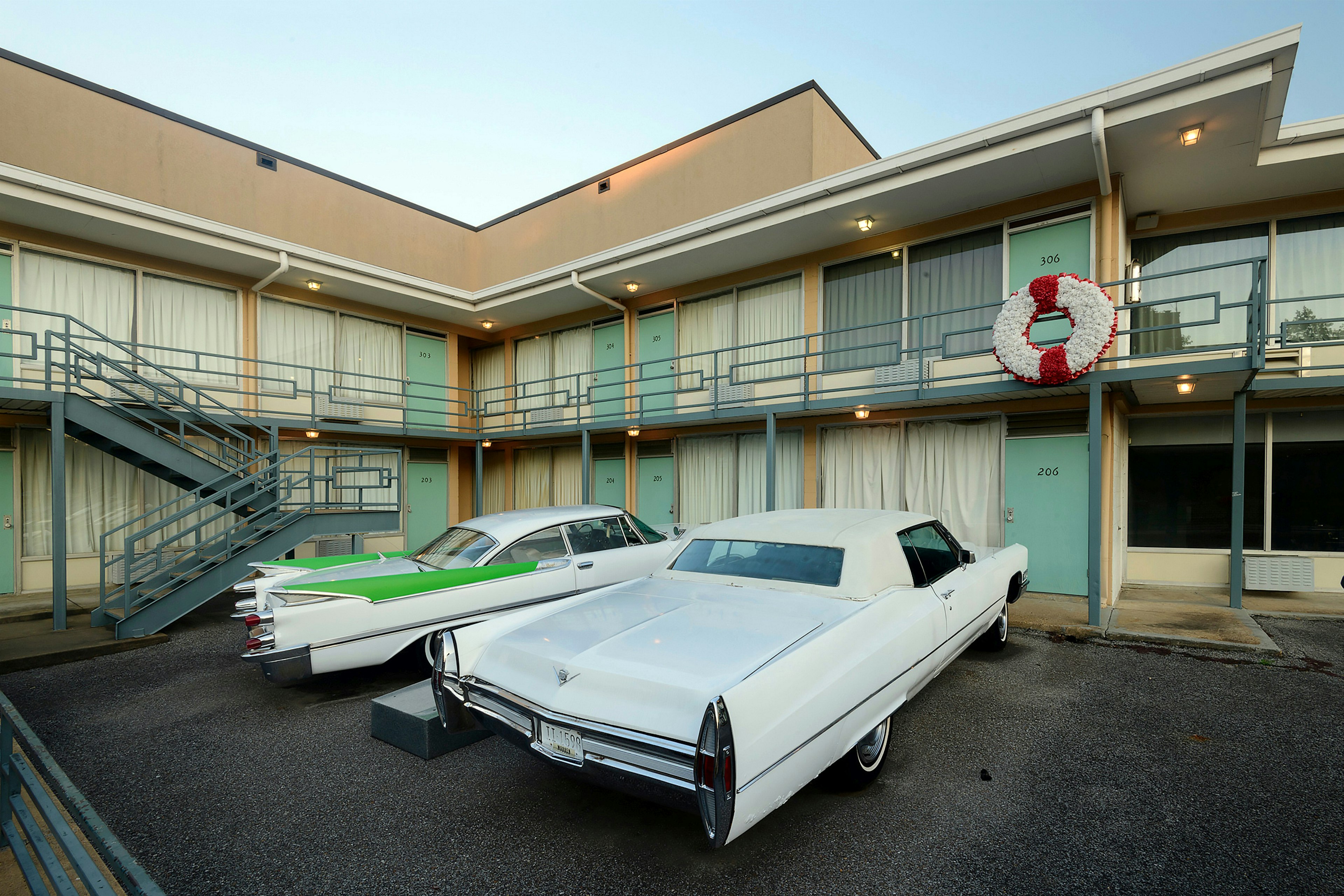 A pair of Cadillacs, one all white and the other white with green fins, are parked outside the balcony of the Lorraine Motel. The scene where Dr. Martin Luther King Jr. was assassinated.