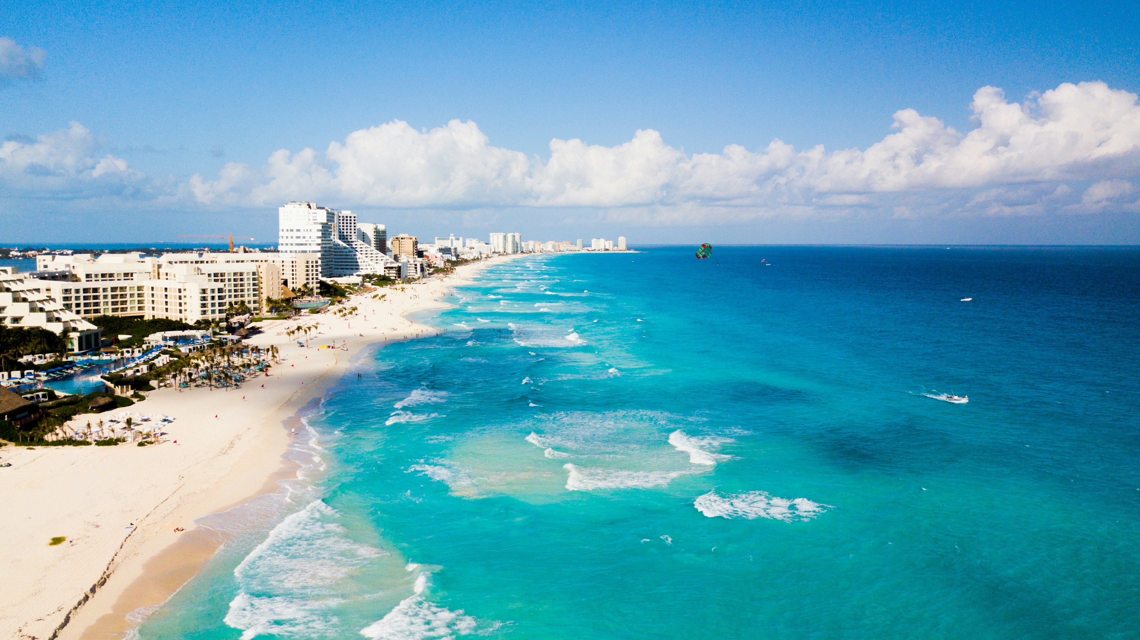 Aerial of Cancun beach on a sunny day with parasailers, swimmers and sunbathers. 