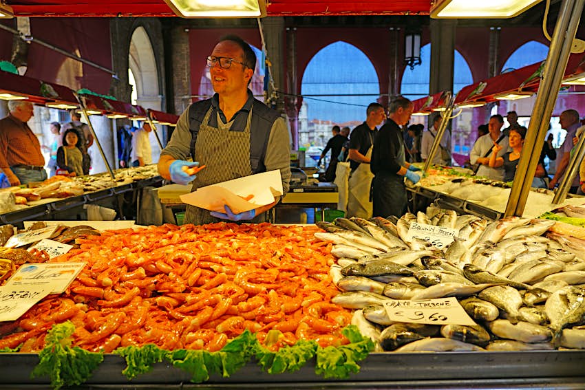A man selling fresh seafood for sale at the Rialto farmers market (Mercato di Rialto) in Venice, near the Rialto Bridge and the Grand Canal.