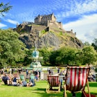 August 2018: People relaxing near Ross Fountain in Princes street gardens, with Edinburgh Castle above.