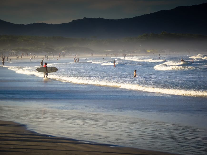 Surfers and swimmers at Barra da Lagoa beach in the late afternoon in Florianópolis, Brazil