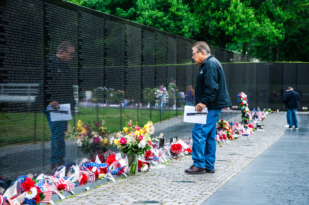shutterstockRF_140277205.jpg A man stands in front of the memorial. Flowers are all along the front of the wall.