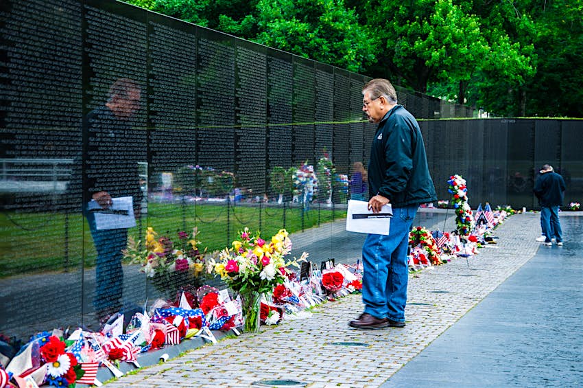 shutterstockRF_140277205.jpg A man stands in front of the memorial. Flowers are all along the front of the wall.