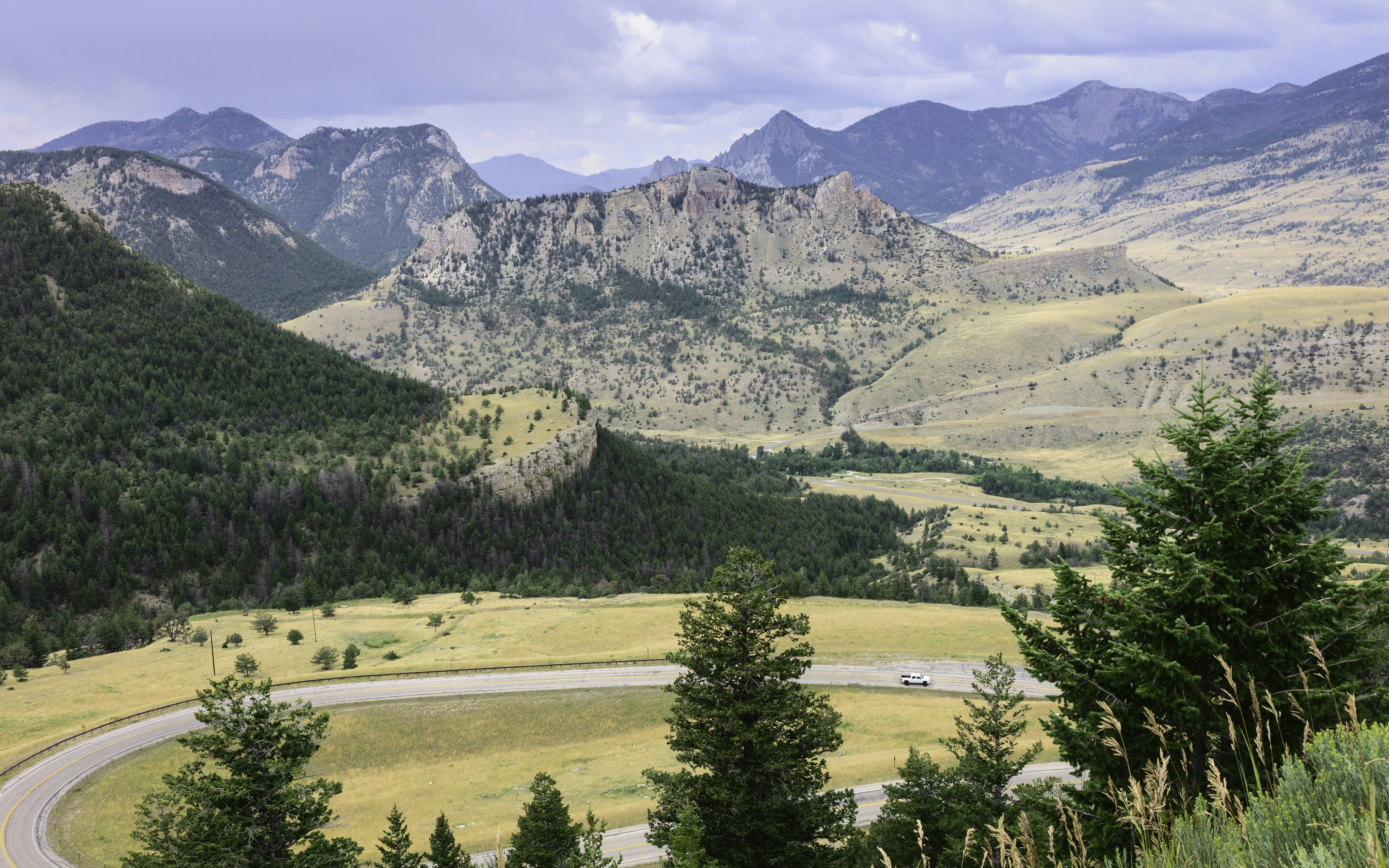 A car follows a winding road among fields with mountains looming overhead