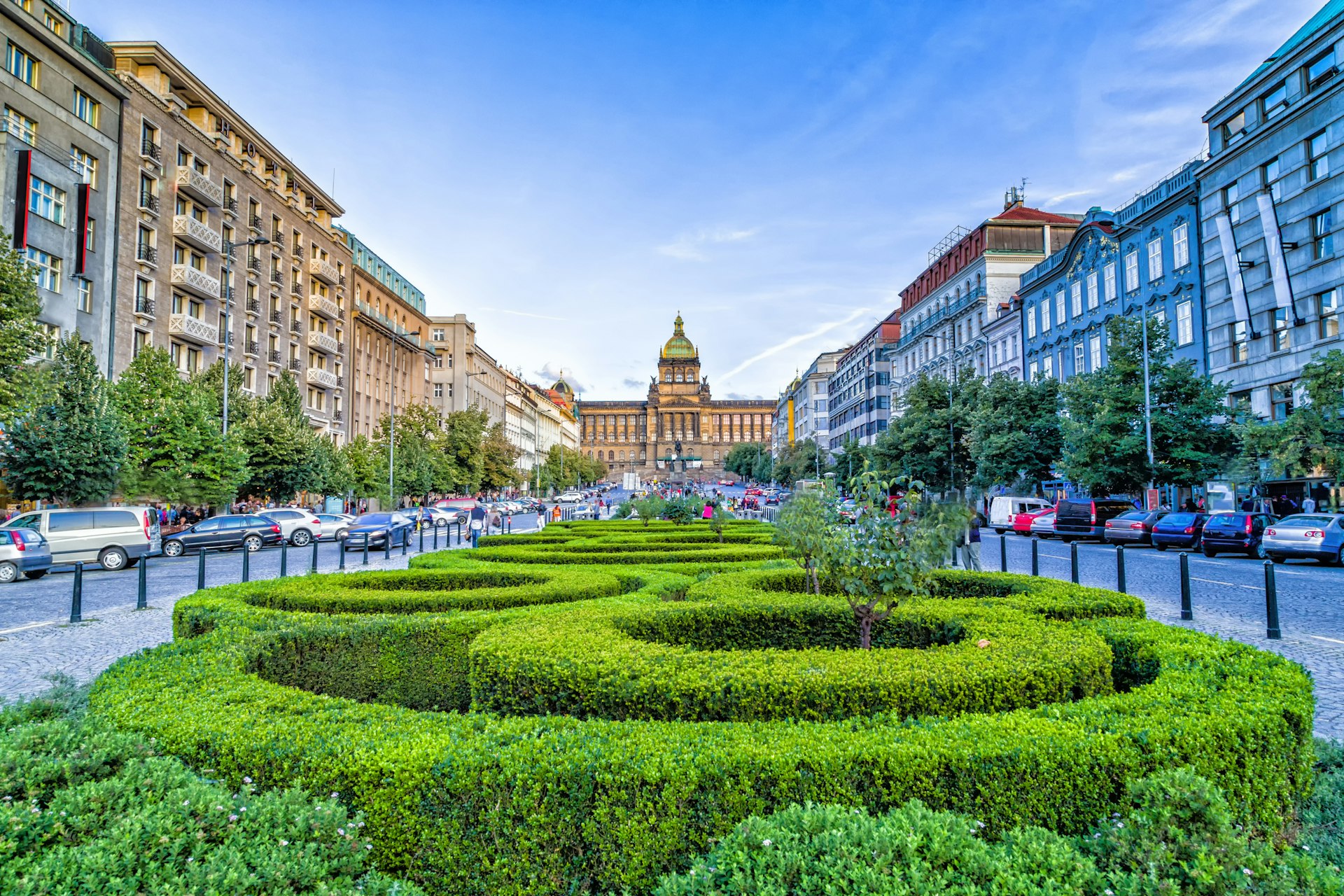 A large rectangular city square with a series of manicured hedges and flower beds.